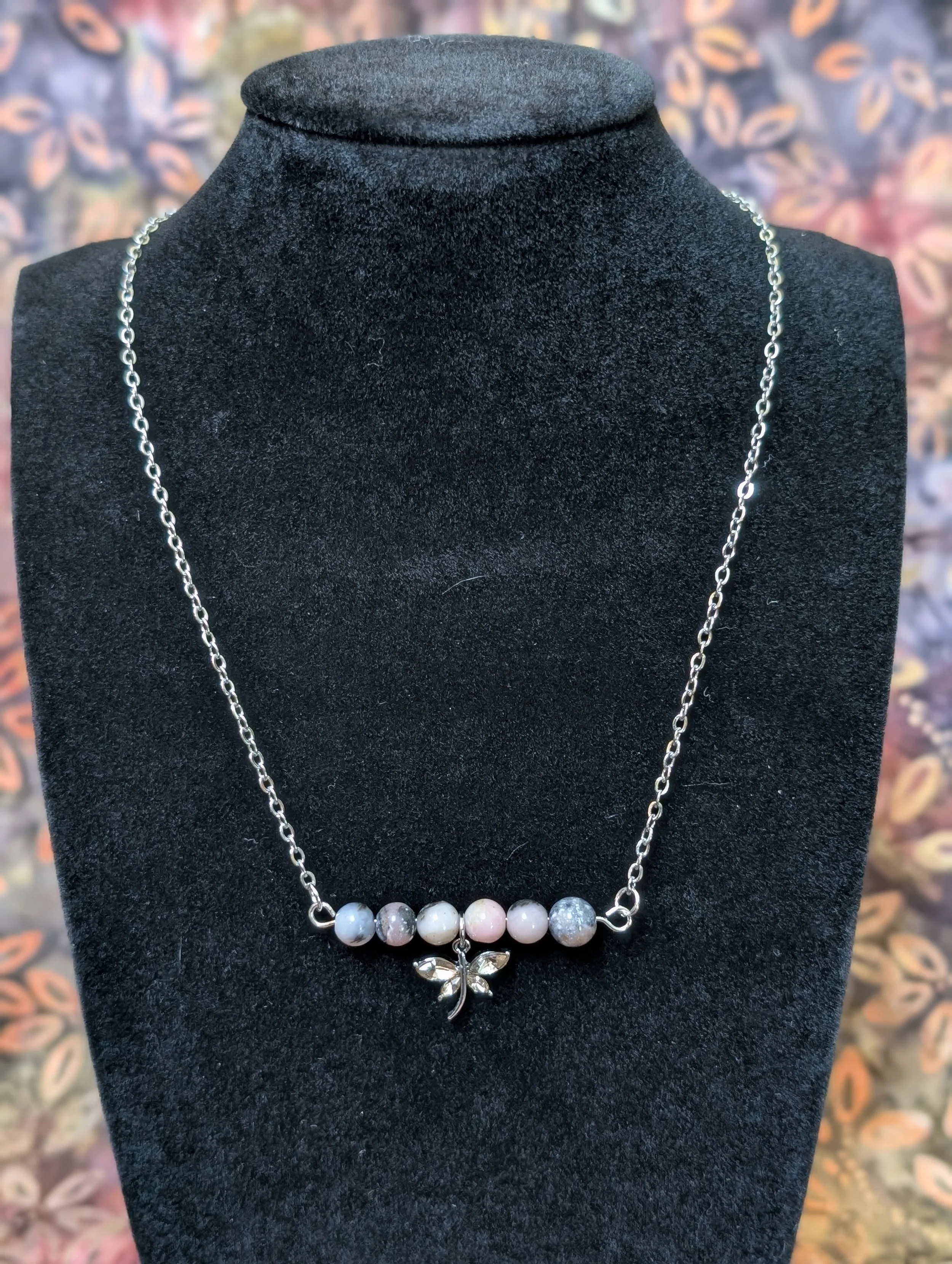 A necklace in Mexican Red Snowflake Obsidian with a pink butterfly accent