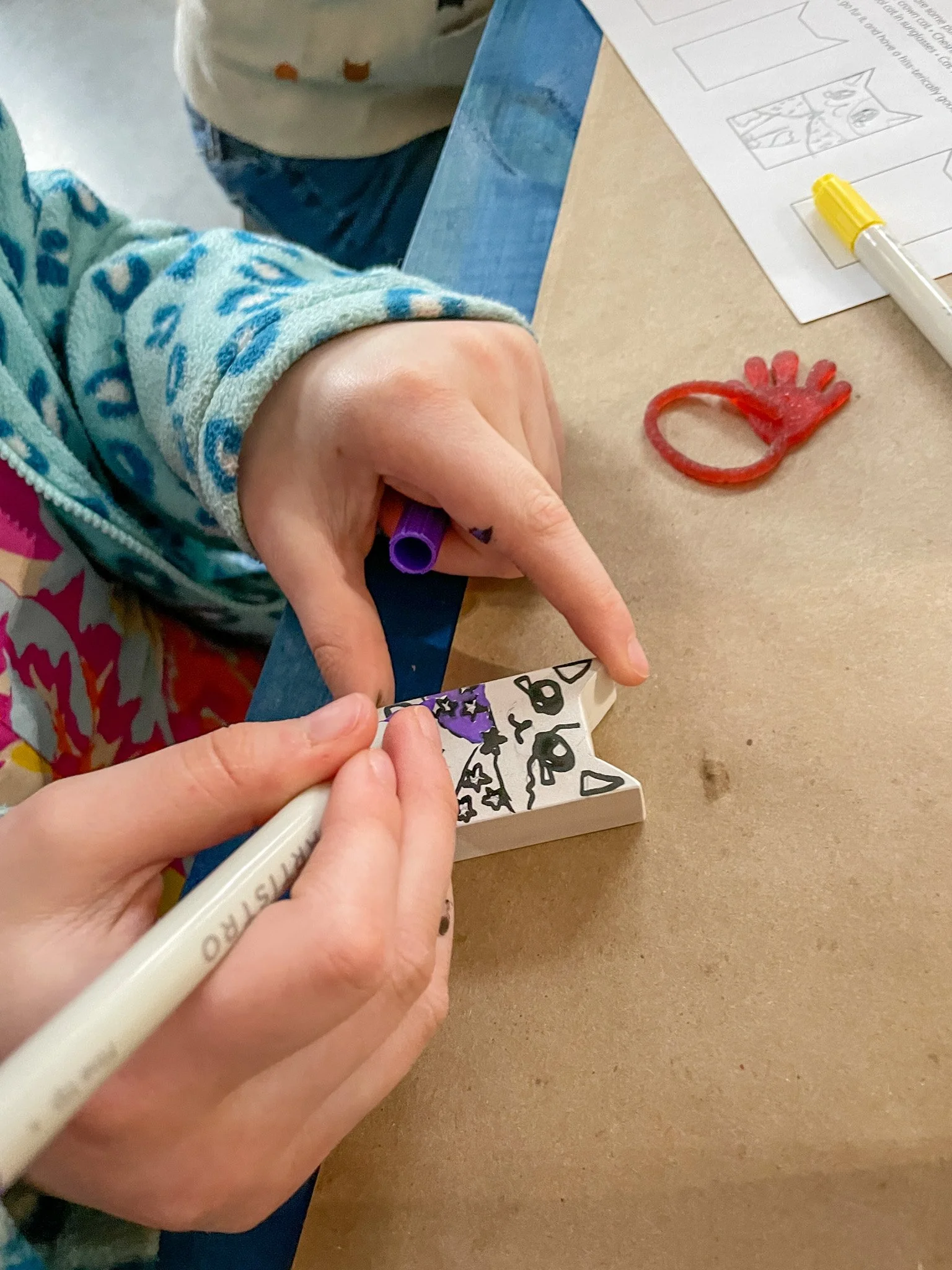 Closeup of a child's hands while they paint their miniature wooden cat figurine