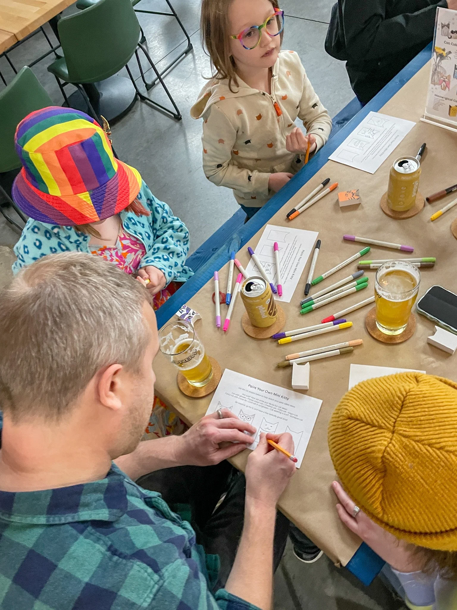 A group of children and an adult sitting at a table with coloring supplies, coloring pages, and drinks, participating in a craft activity.