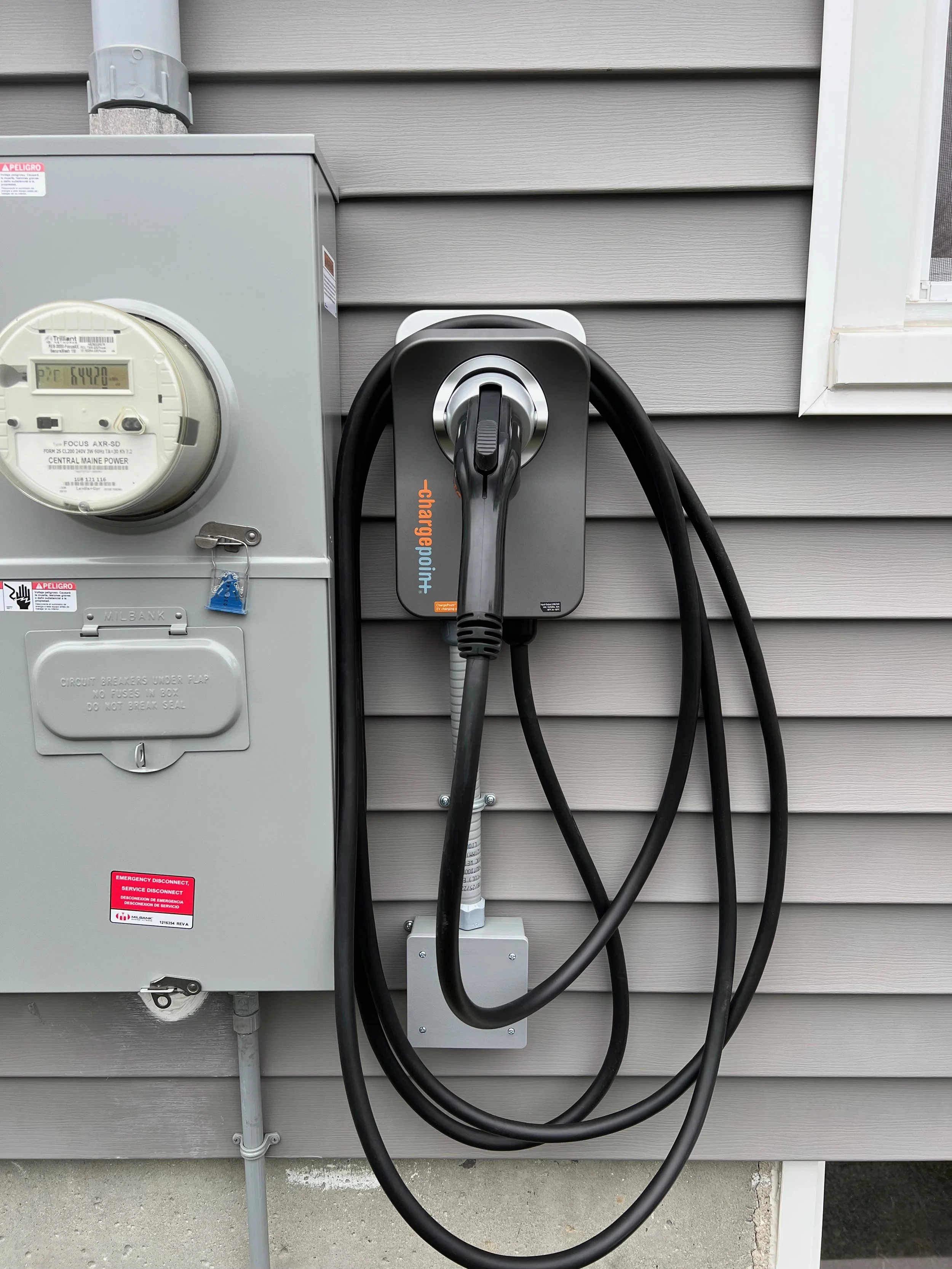 Electric vehicle charging station attached to the exterior wall of a building, with thick black charging cables hanging from it.