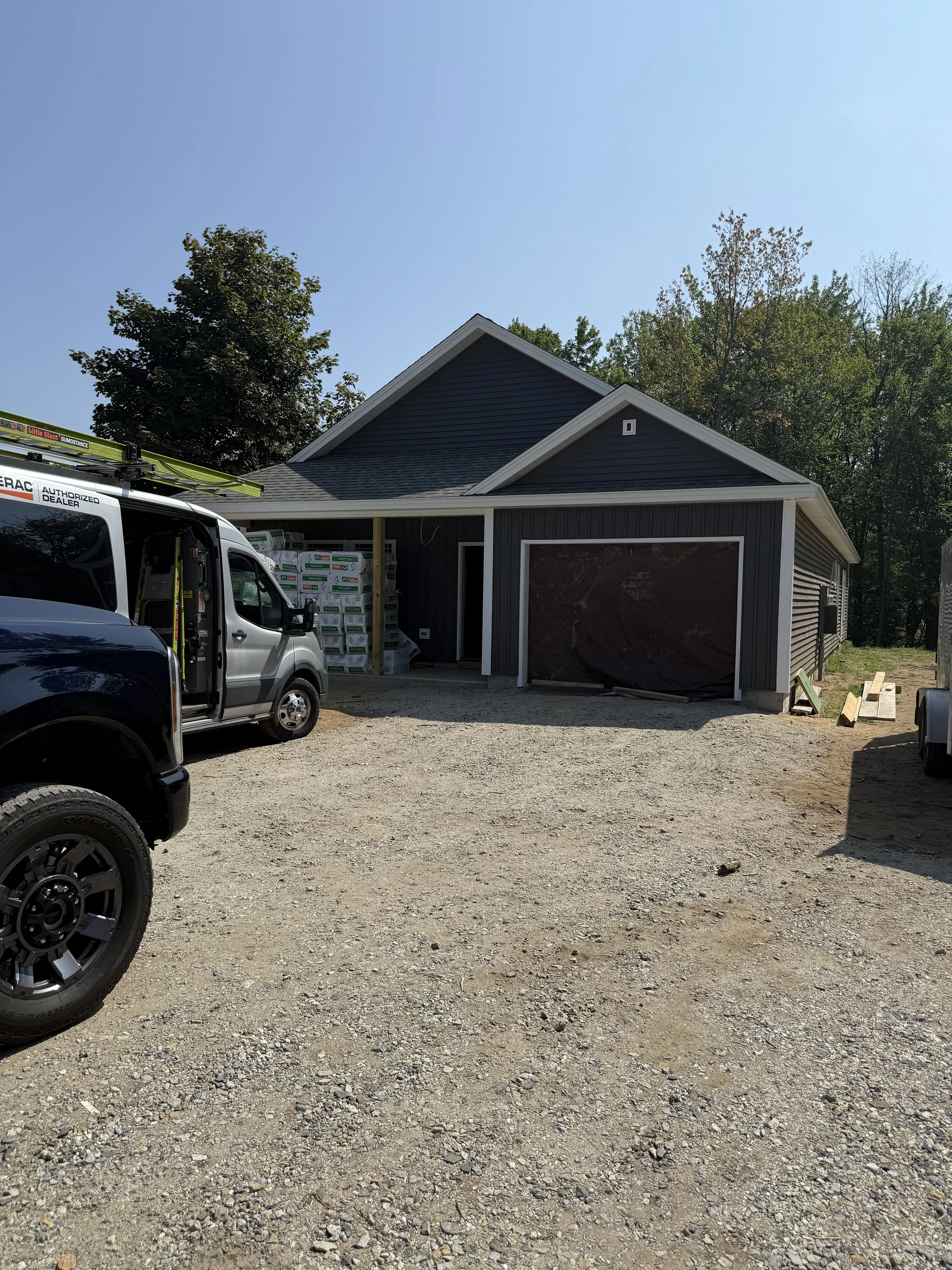 Construction site with a dark gray house, a parked pickup truck, construction materials, and a gravel driveway.