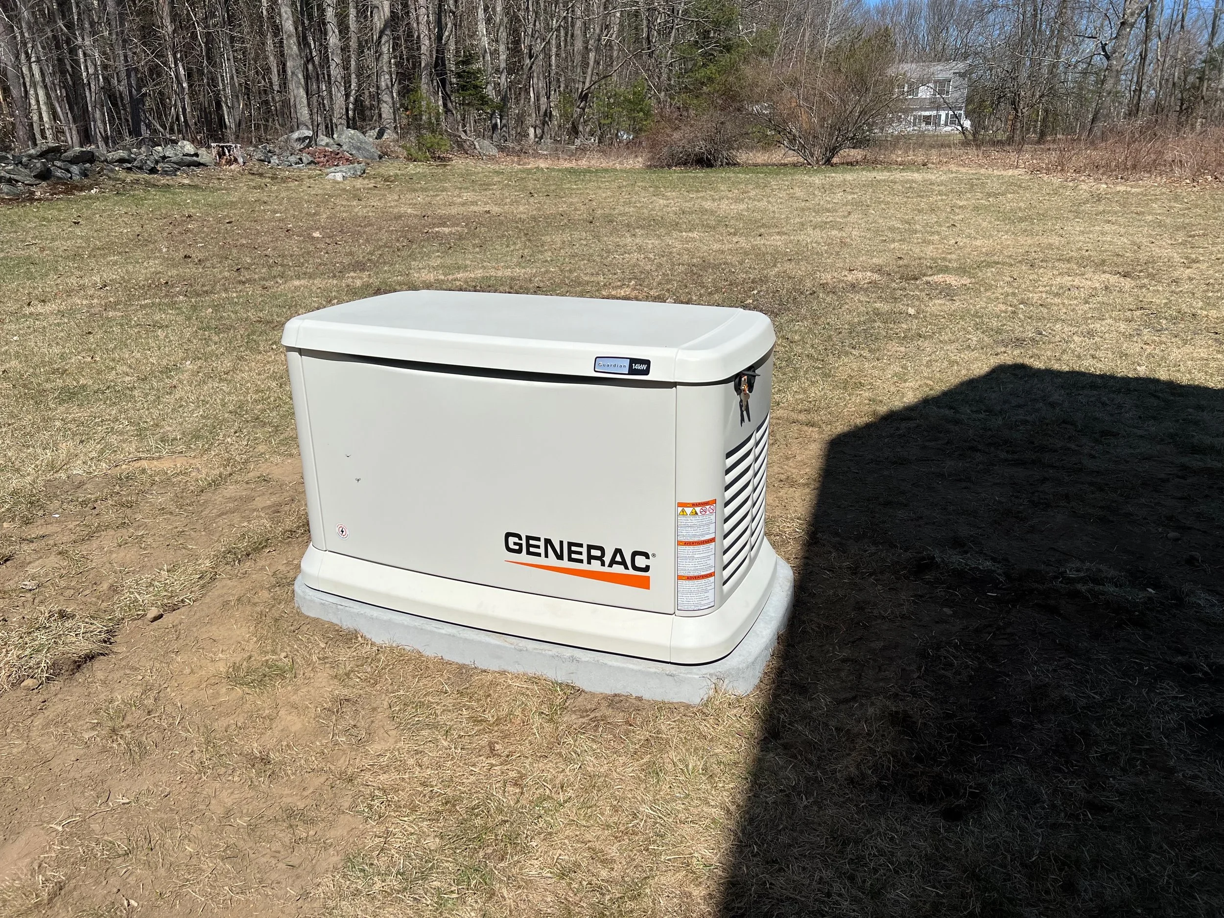 A Generac portable generator on a concrete pad in an open yard with grass, trees, and a house in the background.