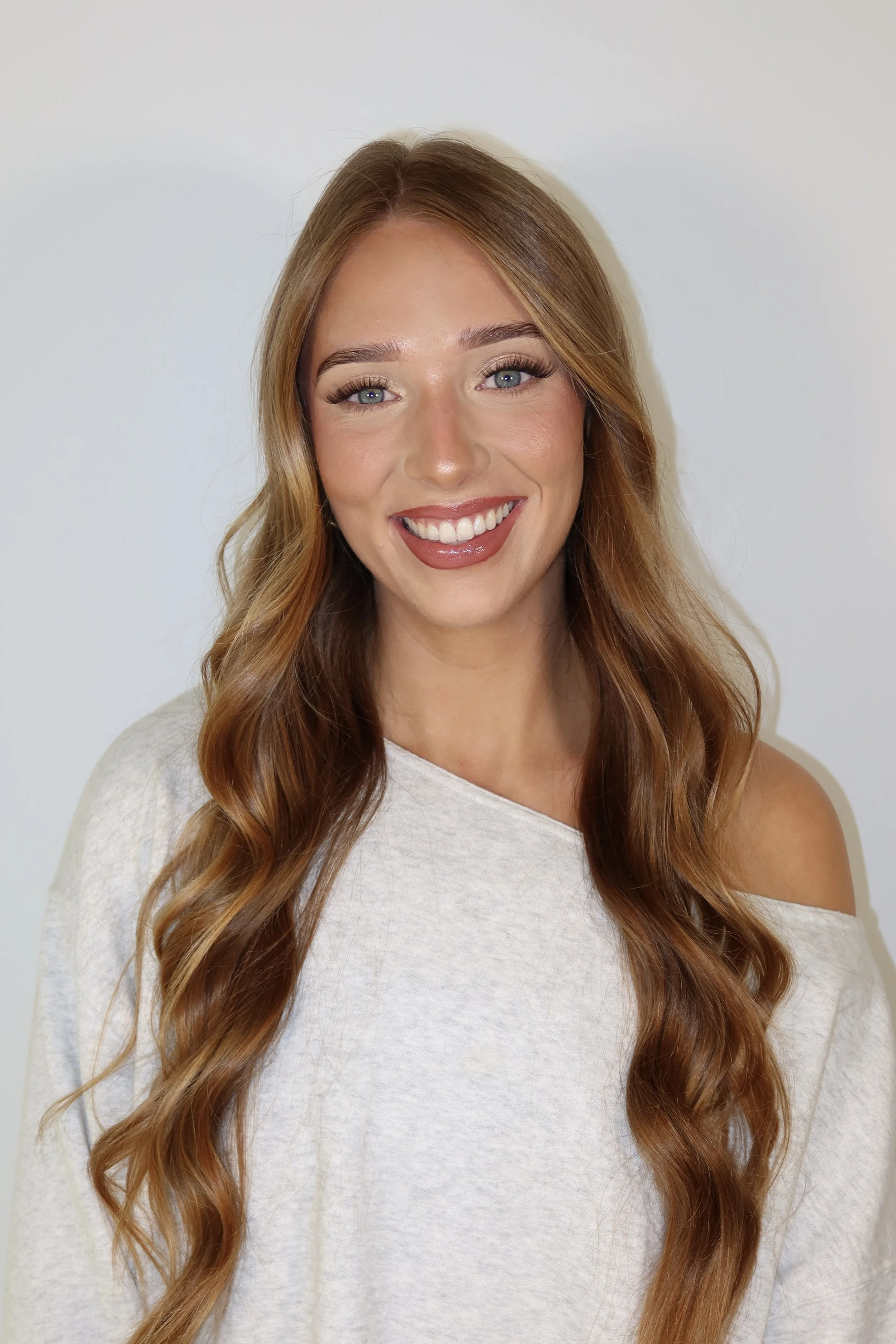 A woman with long, wavy red hair and blue eyes smiling against a plain white background.