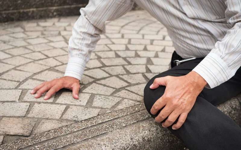 A person in a white striped shirt kneeling on a stone sidewalk, with one hand on the ground and the other on their knee.