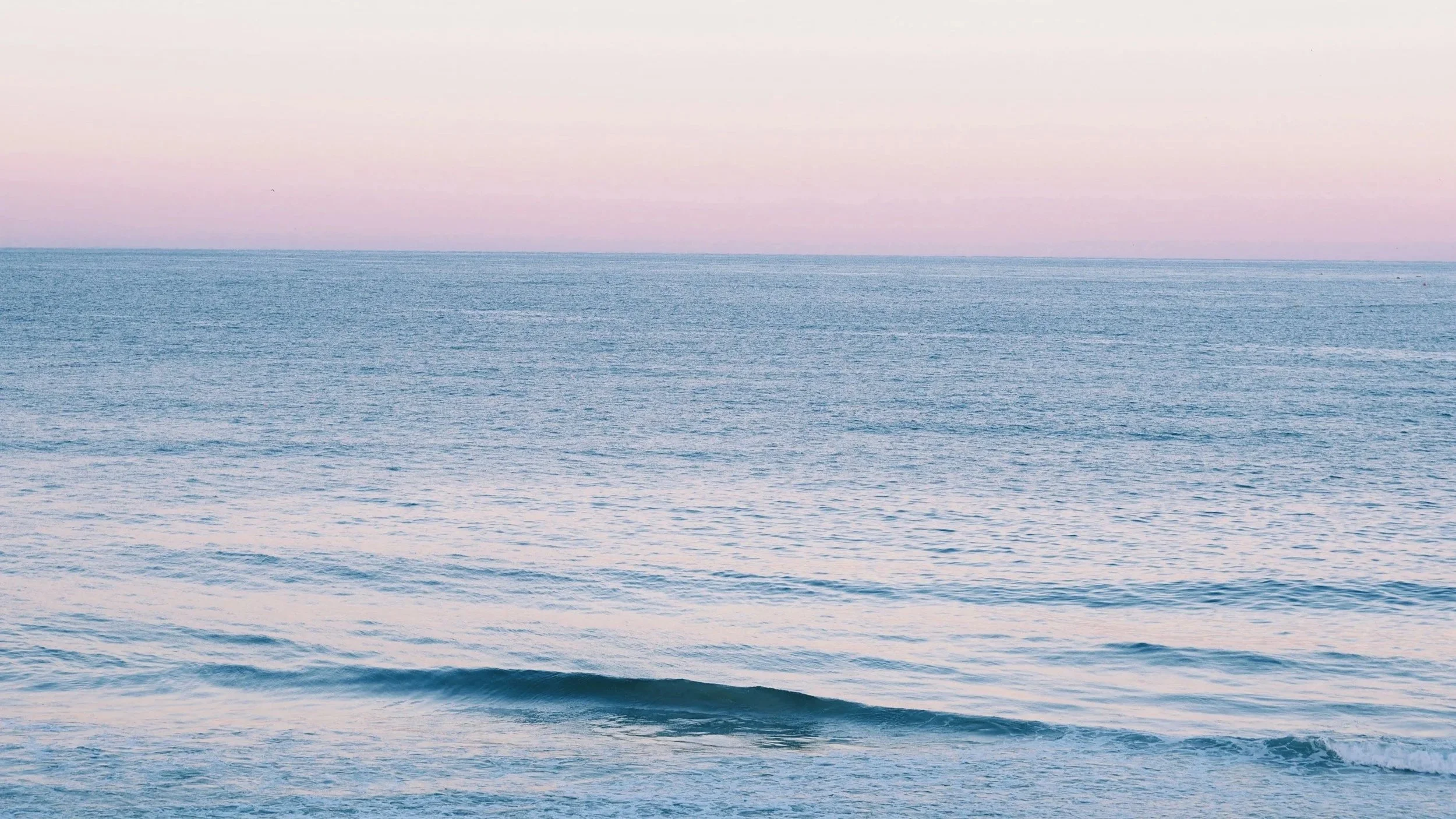 Calm blue ocean with gentle waves beneath a soft pink and lavender sky