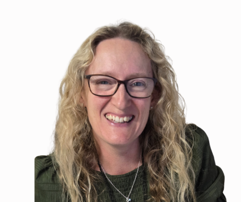 A woman with curly blonde hair, wearing glasses, smiling, and dressed in a dark green top with a necklace, against a white background.