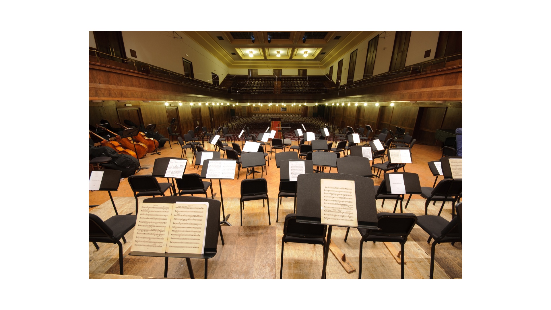 Empty concert hall with music stands, chairs, and string instruments, prepared for an orchestral performance.