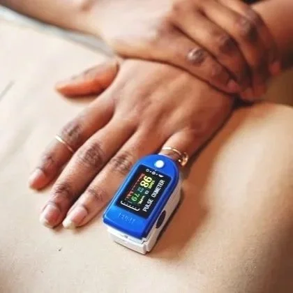 Close-up of a person's hand holding another person's hand, with a pulse oximeter on their finger displaying oxygen saturation and pulse rate.