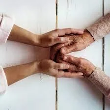 Two pairs of hands, one pair of younger hands and one pair of older hands, interlocked in a show of support and connection on a white wooden surface.