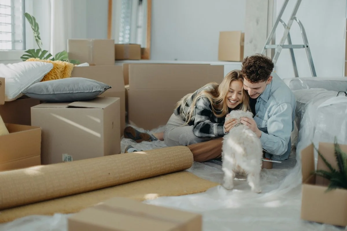 A couple cuddles their dog while surrounded by moving boxes, representing the benefits of dog training before a big move