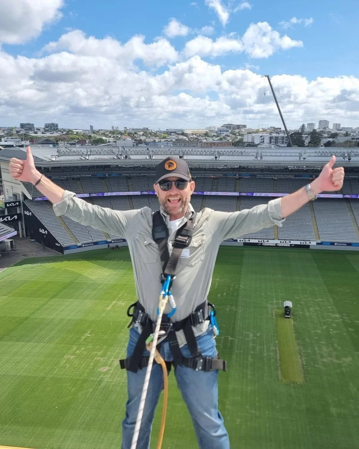Brent the tour guide on the Eden Park roof top tour in a harness with the North Stand and Auckland City in the background