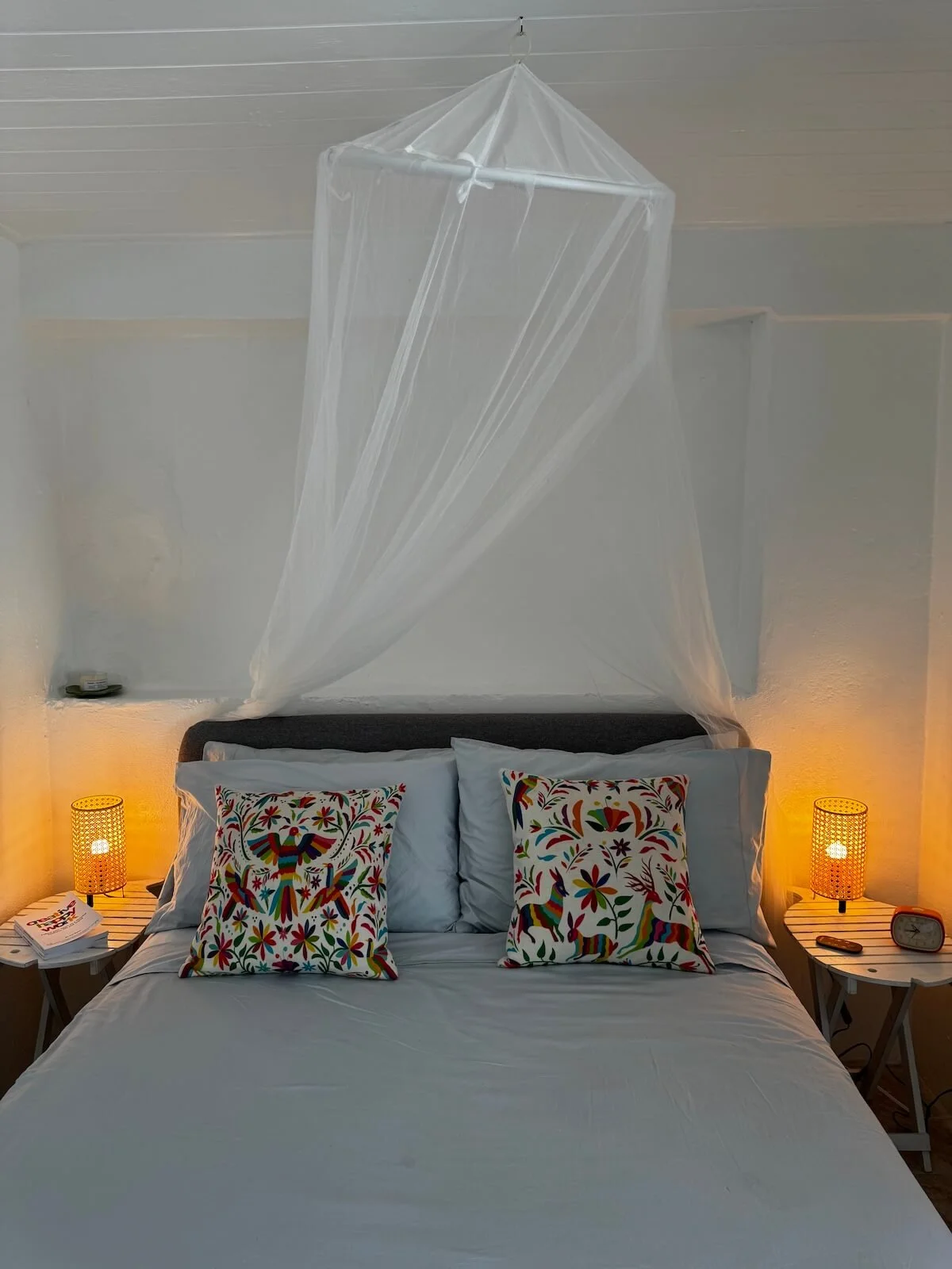 A comfortable double bed at the studio apartment for The Sea Change Retreat with a mosquito net and lights with a copy of Creative Happy Work by Kat Byles on the bed side table.