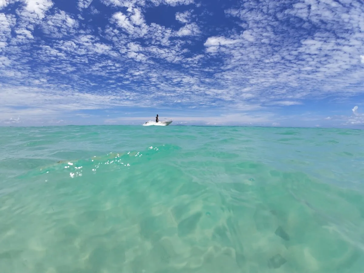 A person riding a speedboat on clear turquoise water beneath a partly cloudy blue sky.