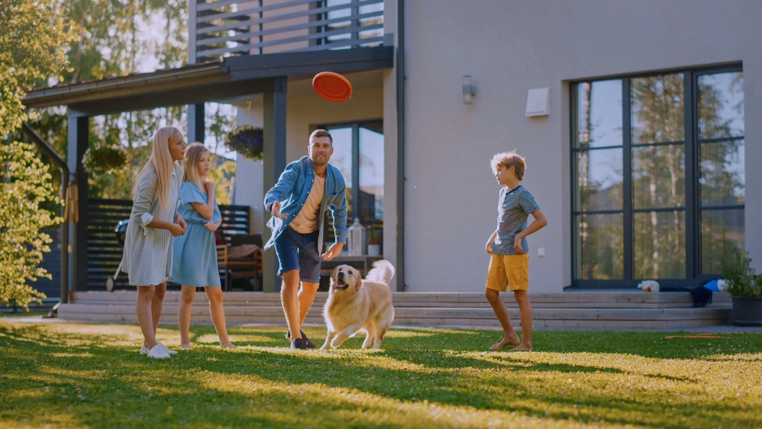 Happy family playing frisbee in their backyard with kids and a dog — symbolizing joyful home life supported by GoodMaids household services.