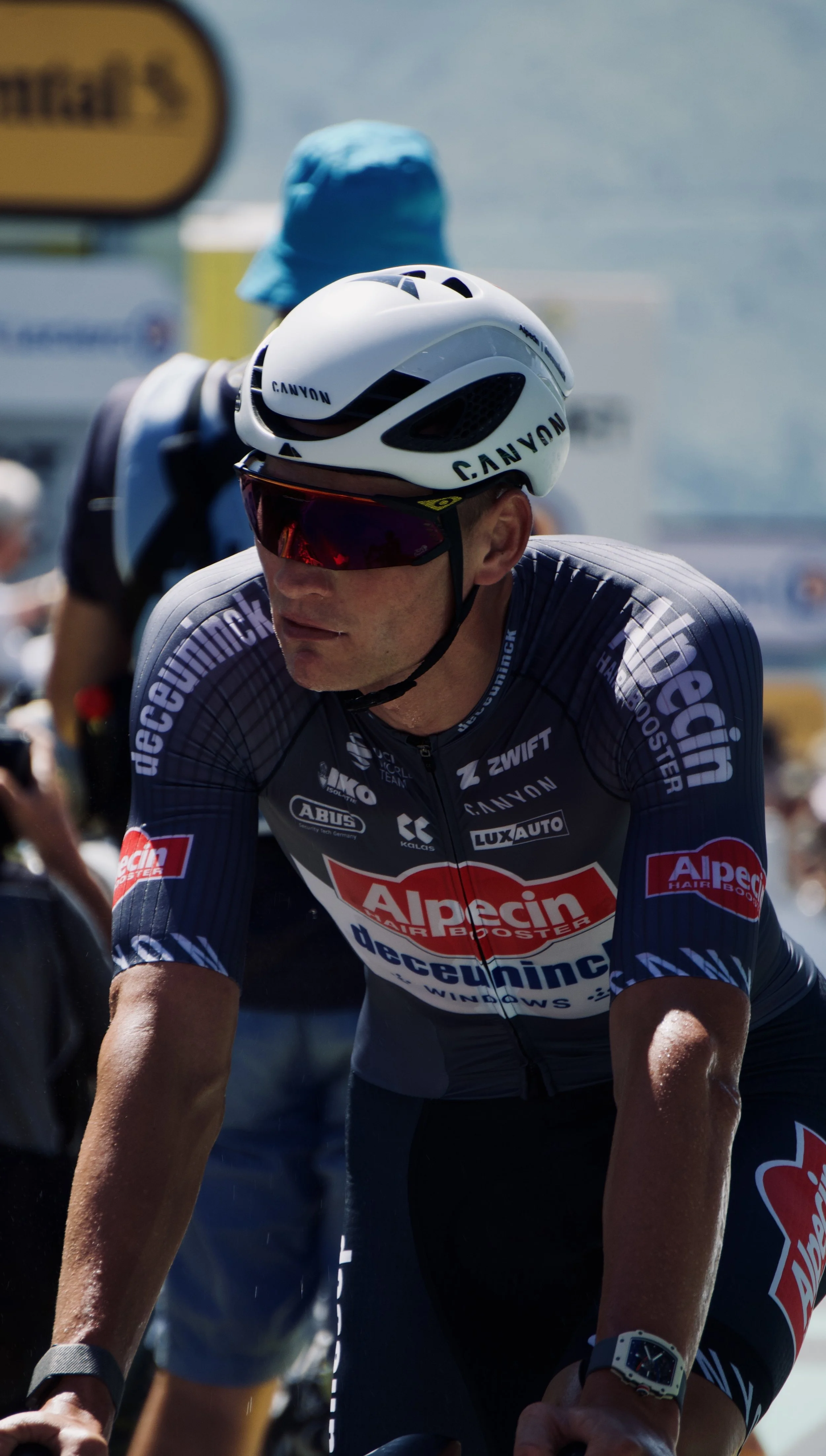 Cycliste en tenue de course, portant un casque blanc avec le logo CANYON et des lunettes de soleil, lors d'une compétition de cyclisme sur route.