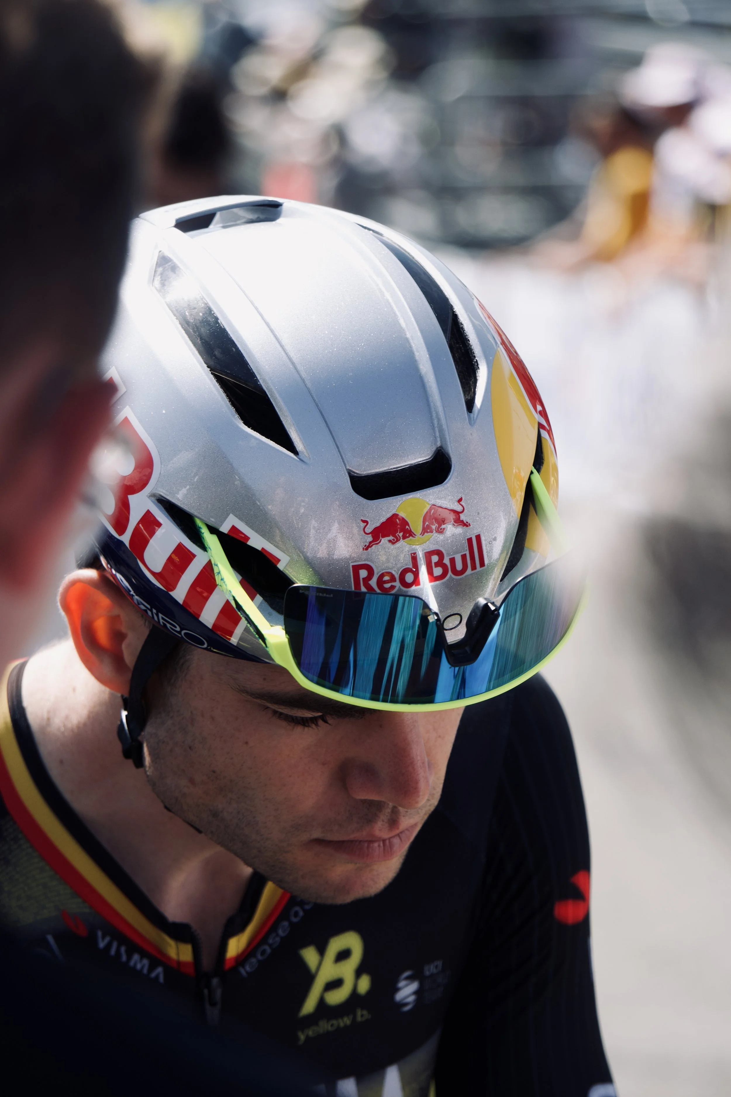 Un cycliste portant un casque avec le logo Red Bull, vue de près avec un focus sur le visage en dessous, en vêtements de course.
