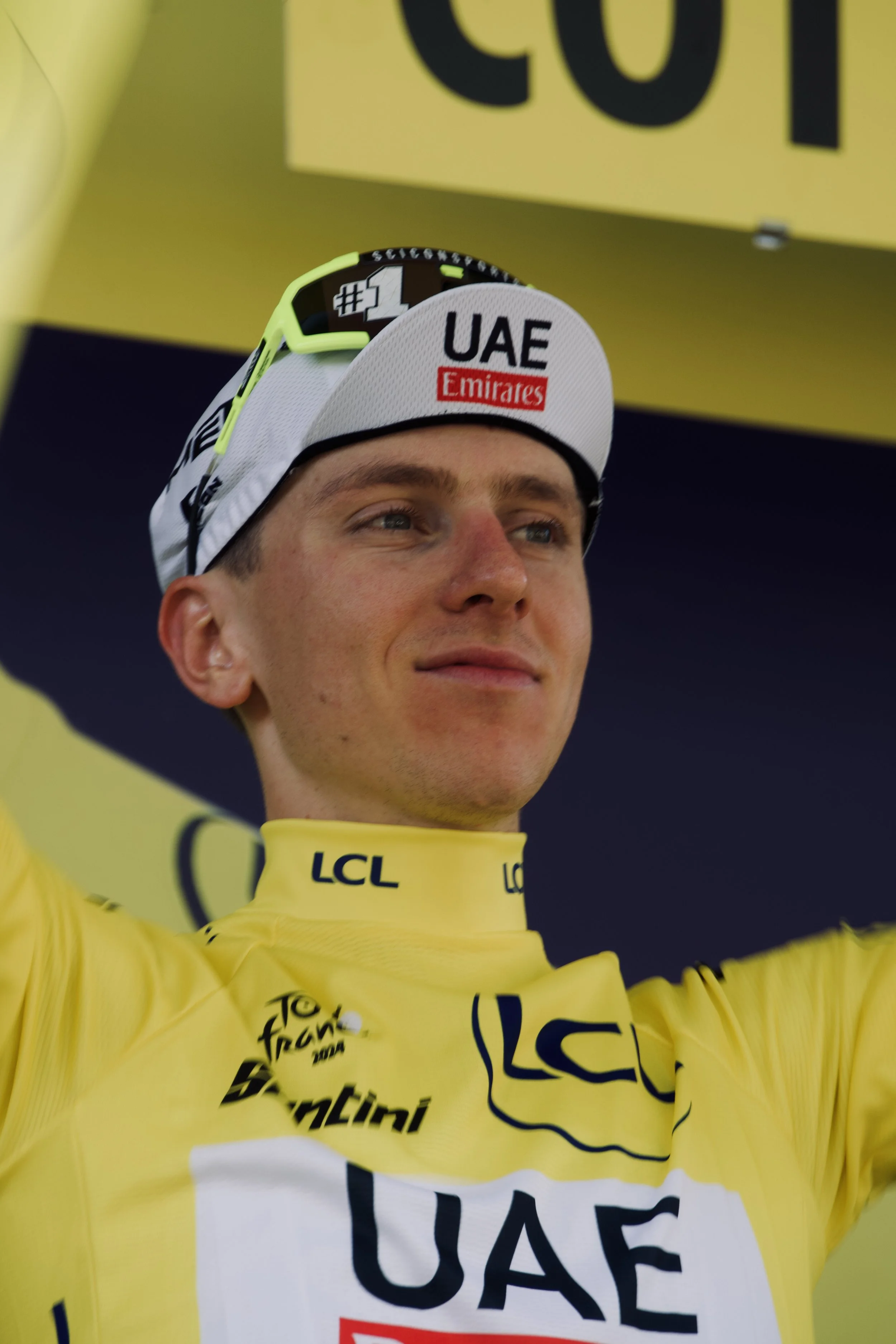 Cycliste en uniforme jaune avec logo LCL et UAE Emirates, portant une casquette blanche avec la mention UAE, célébrant une victoire.