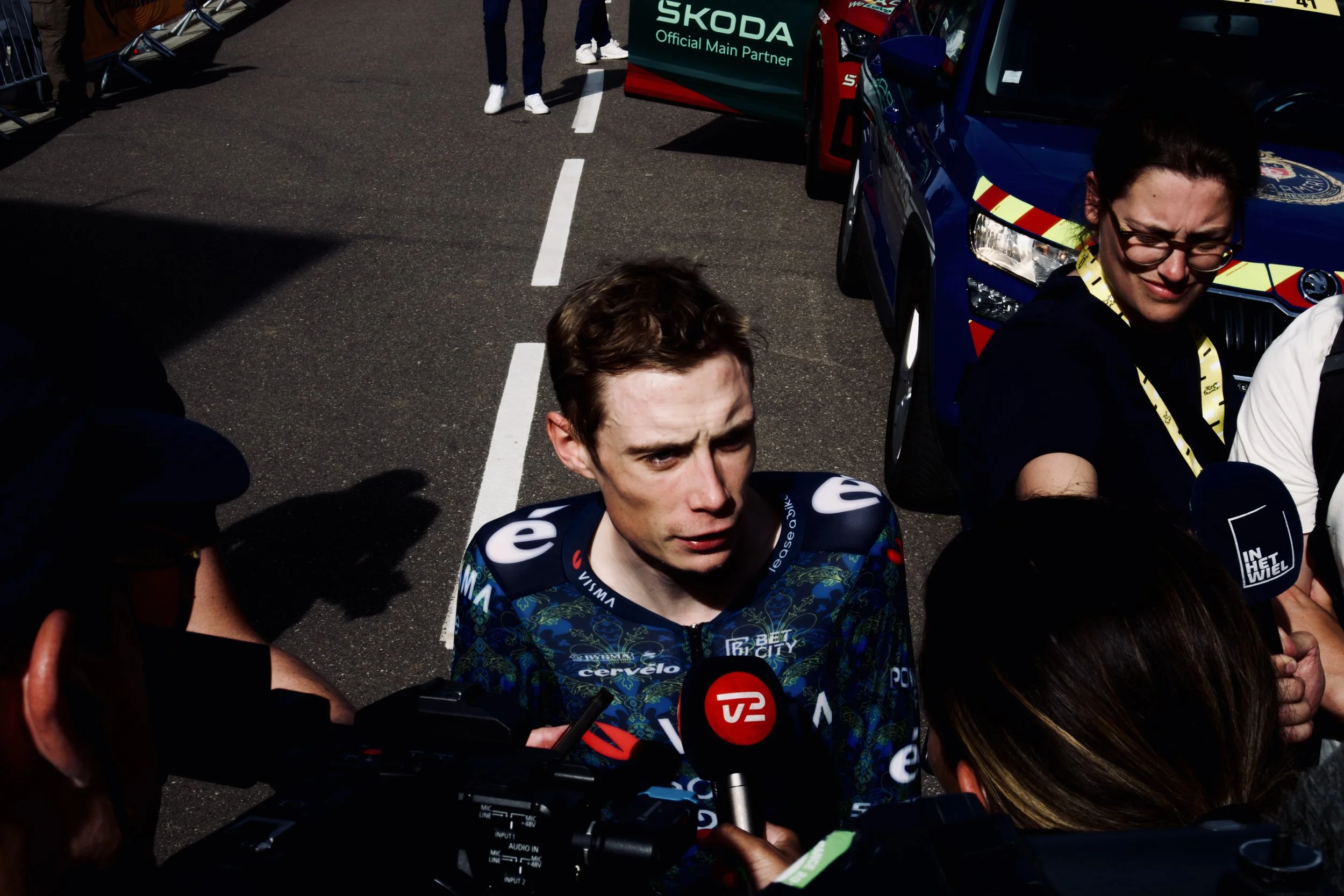 Un pilote de course en train d'être interviewé par des journalistes devant une voiture de course en dehors d'un circuit.