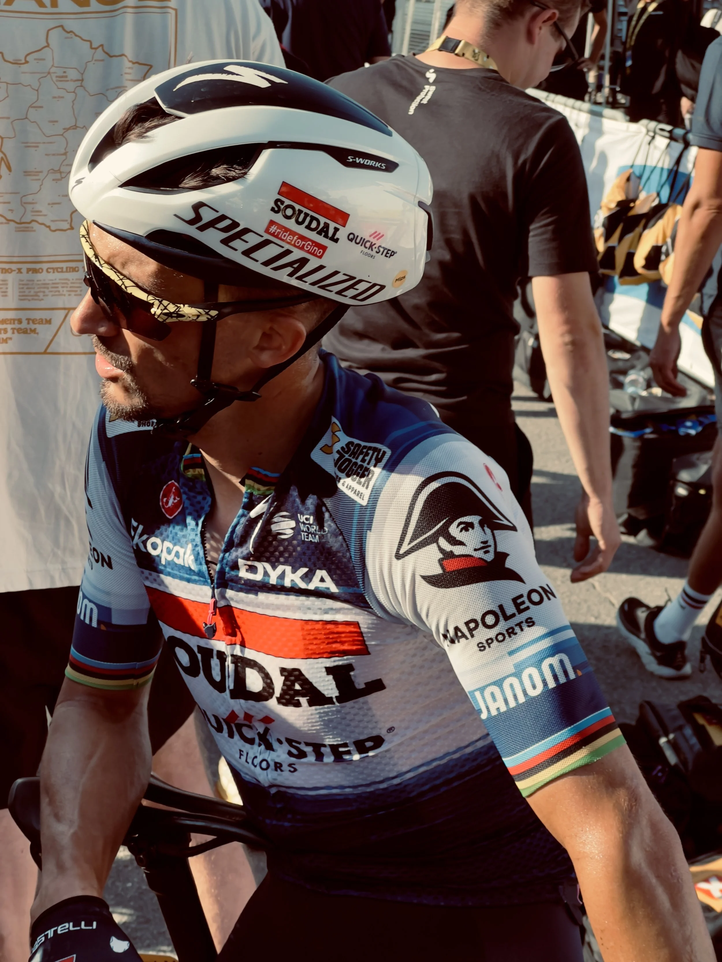 Cycliste portant un casque blanc avec le logo Specialized, vêtement de cyclisme avec le logo Pudal, en plein contexte de course ou d'événement sportif.