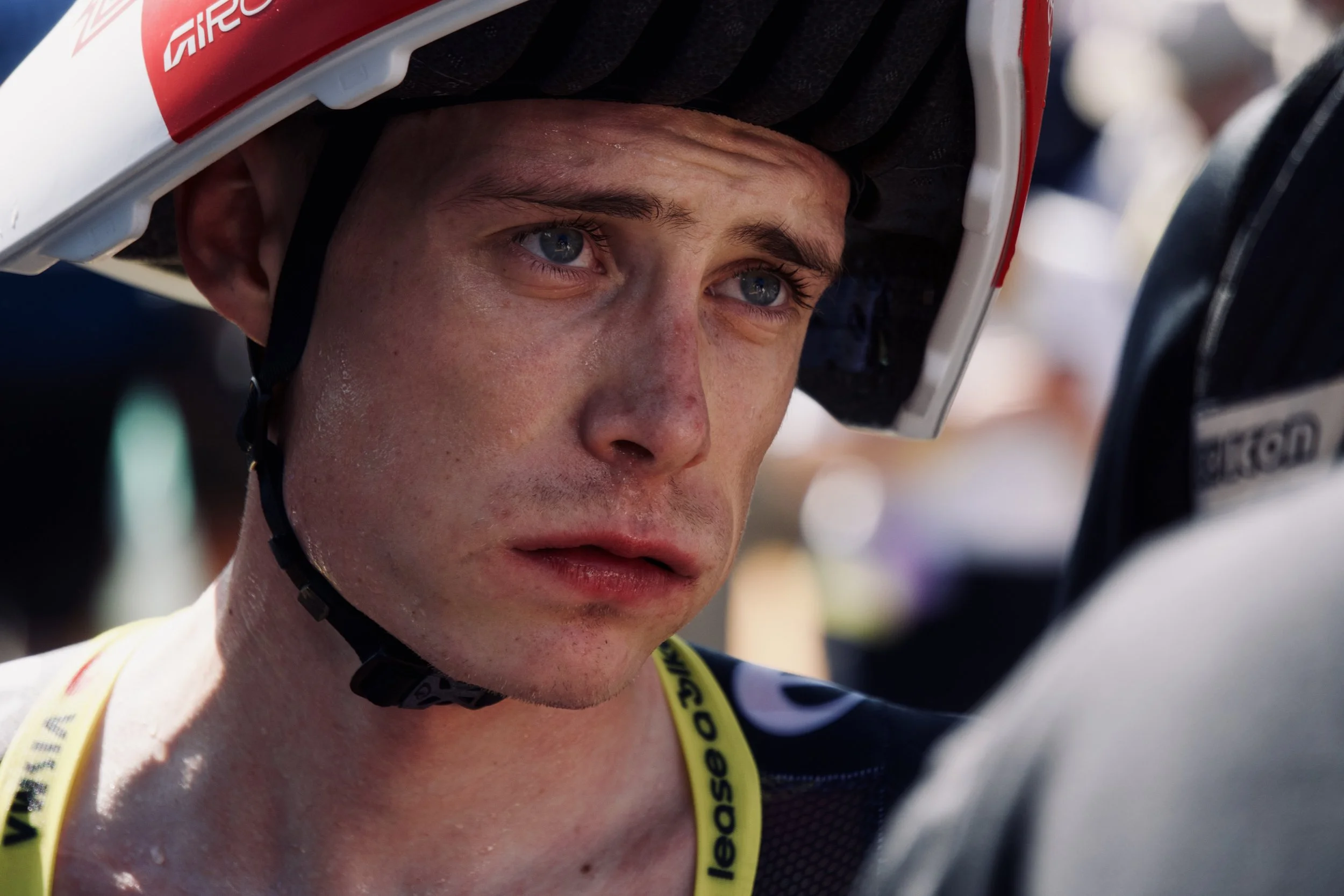 Un homme portant un casque de moto et un maillot de course, semblant concentré et fatigué.