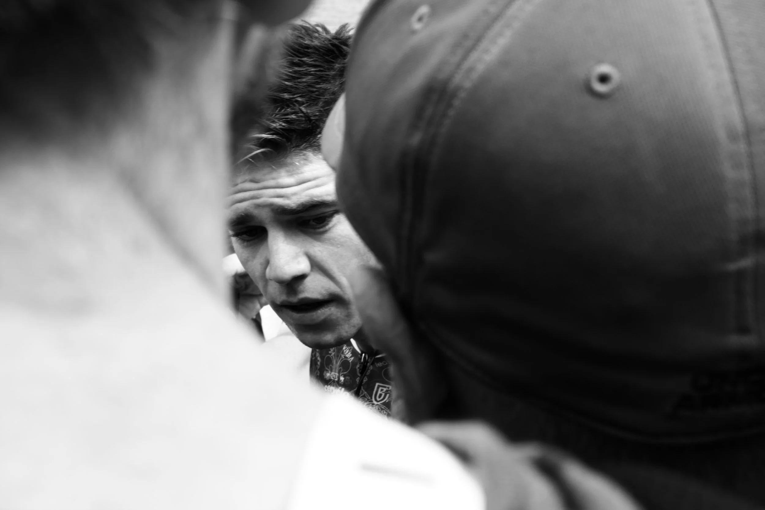 Un homme semble concentré, entouré de plusieurs personnes lors d'une scène en noir et blanc.