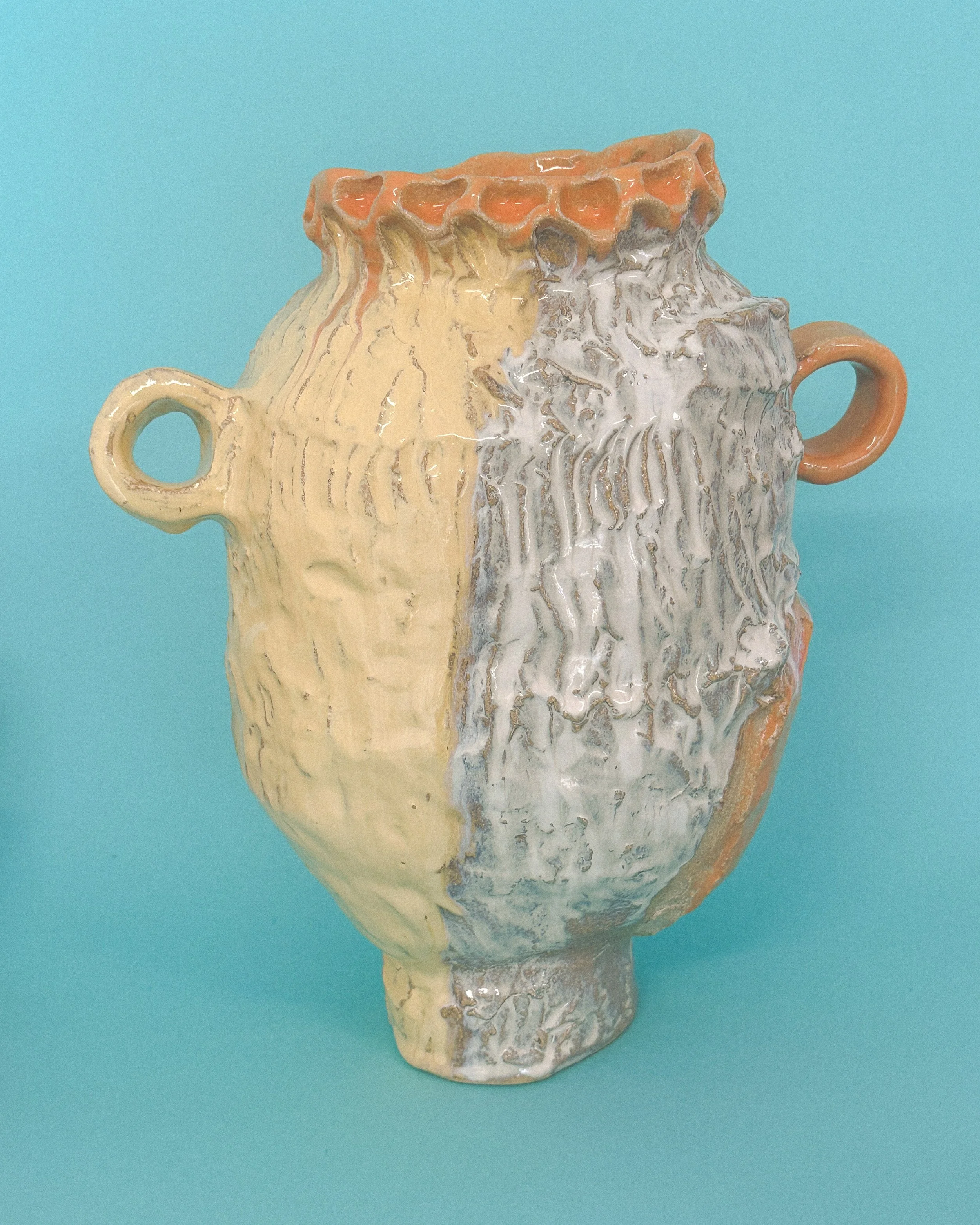 One-of-a-kind handmade ceramic vase with textured surface and layered white, cream and peach glazes, photographed on a blue background.