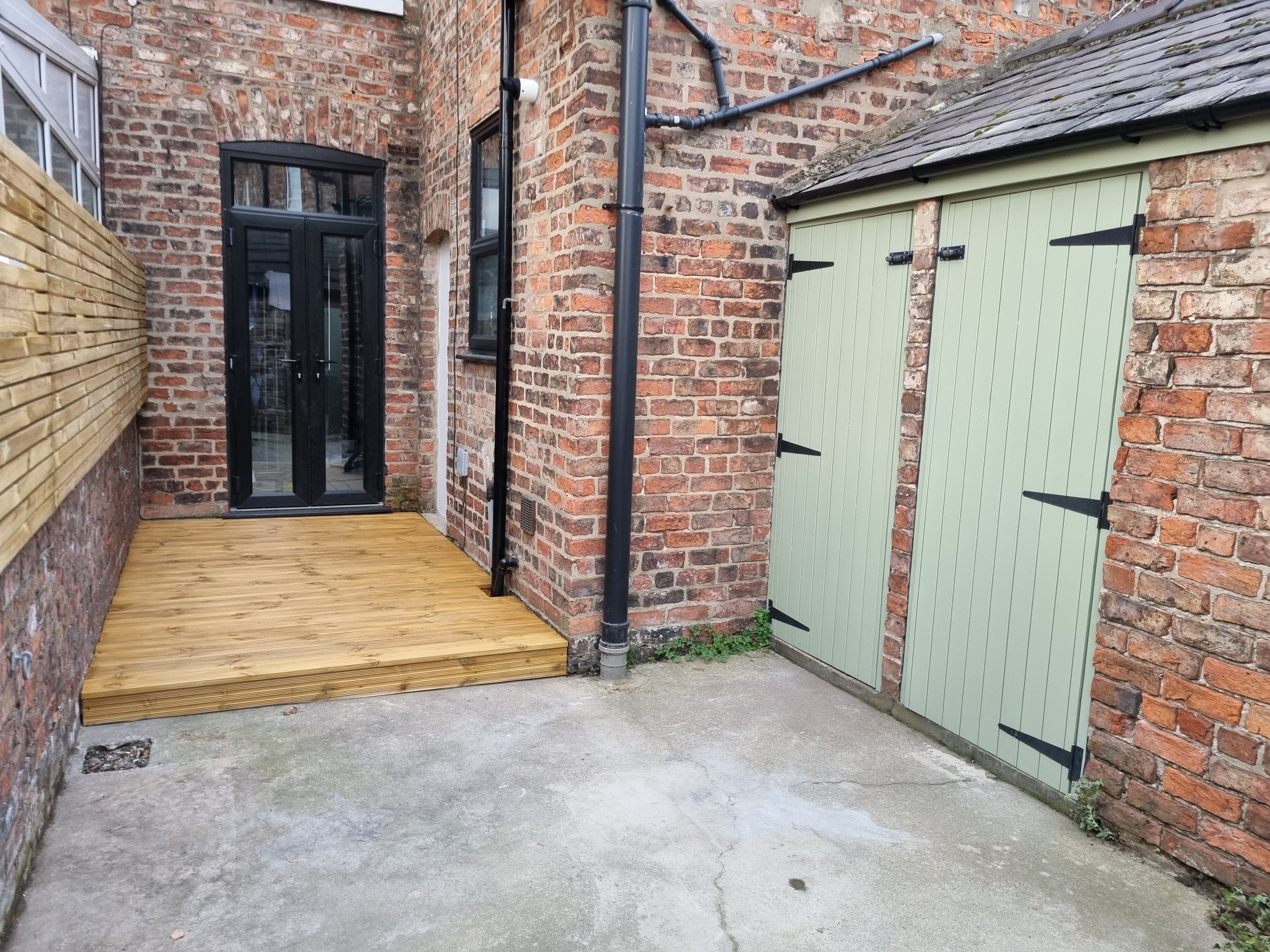 Terrace house, backyard (The Groves). This exterior makeover features a stylish combination of modern and traditional elements. The uPVC French doors and window have been finished in a sleek black, creating a striking contrast against the rustic red 
