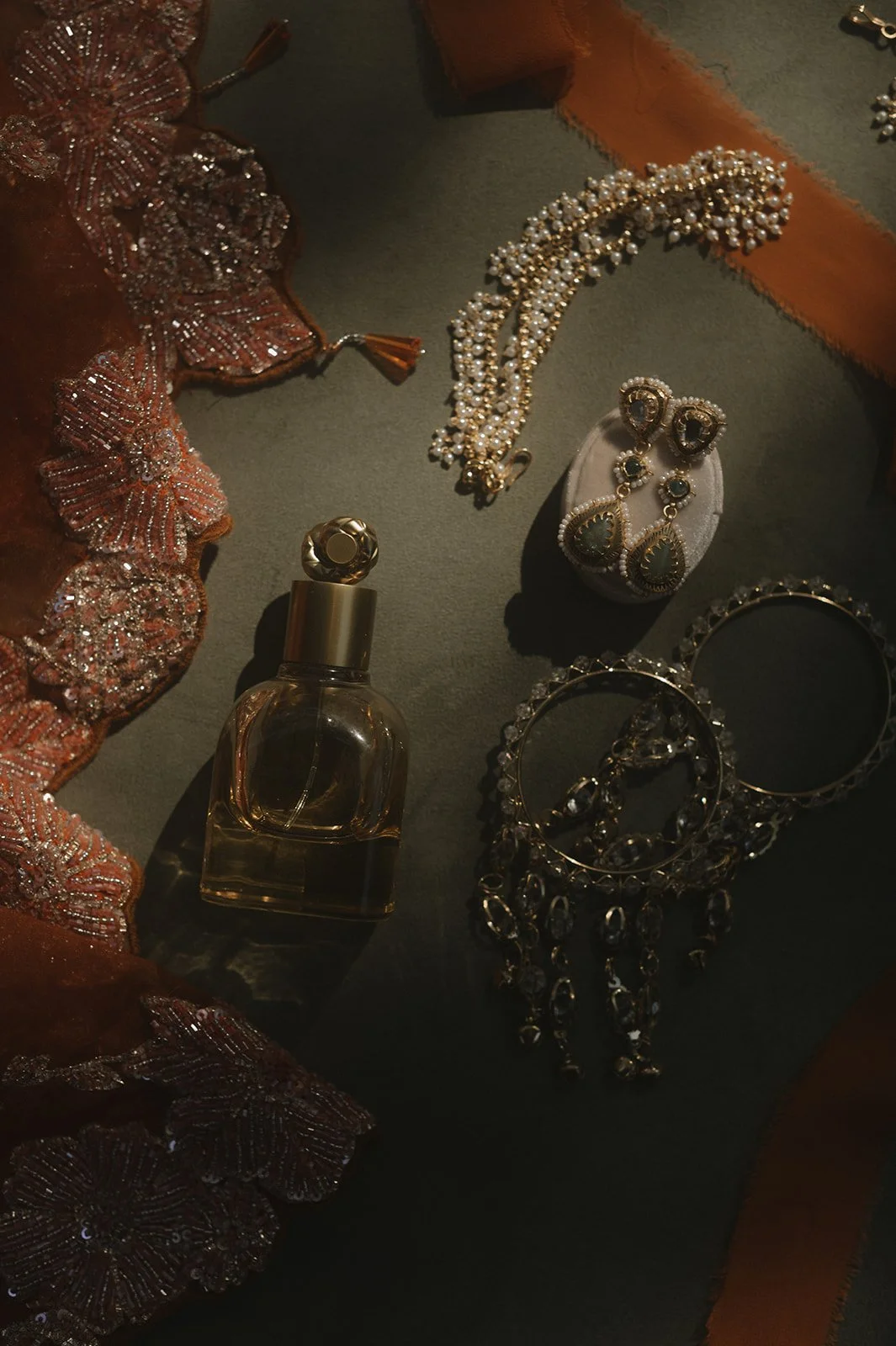 Jewelry and perfume on a dark surface, including pearl necklace, earrings, bracelets, and a perfume bottle.