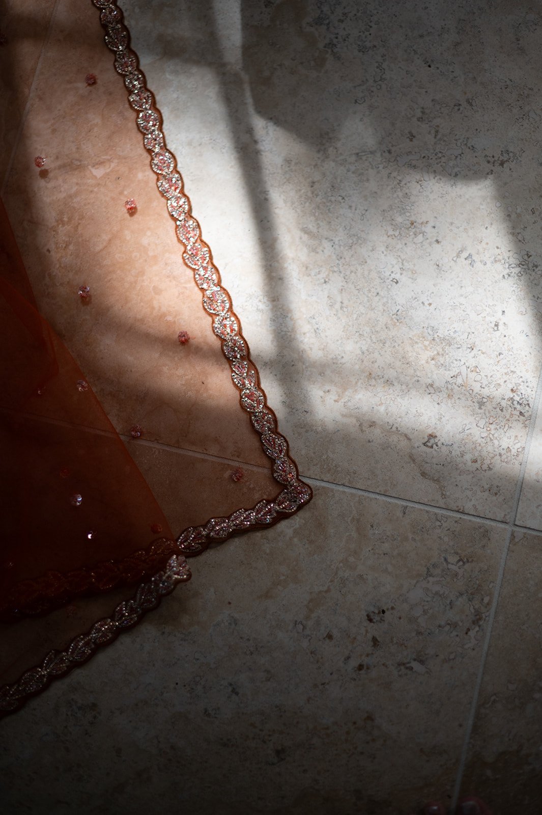 A decorative piece of fabric with a beaded trim and small jewel embellishments on a tiled floor.