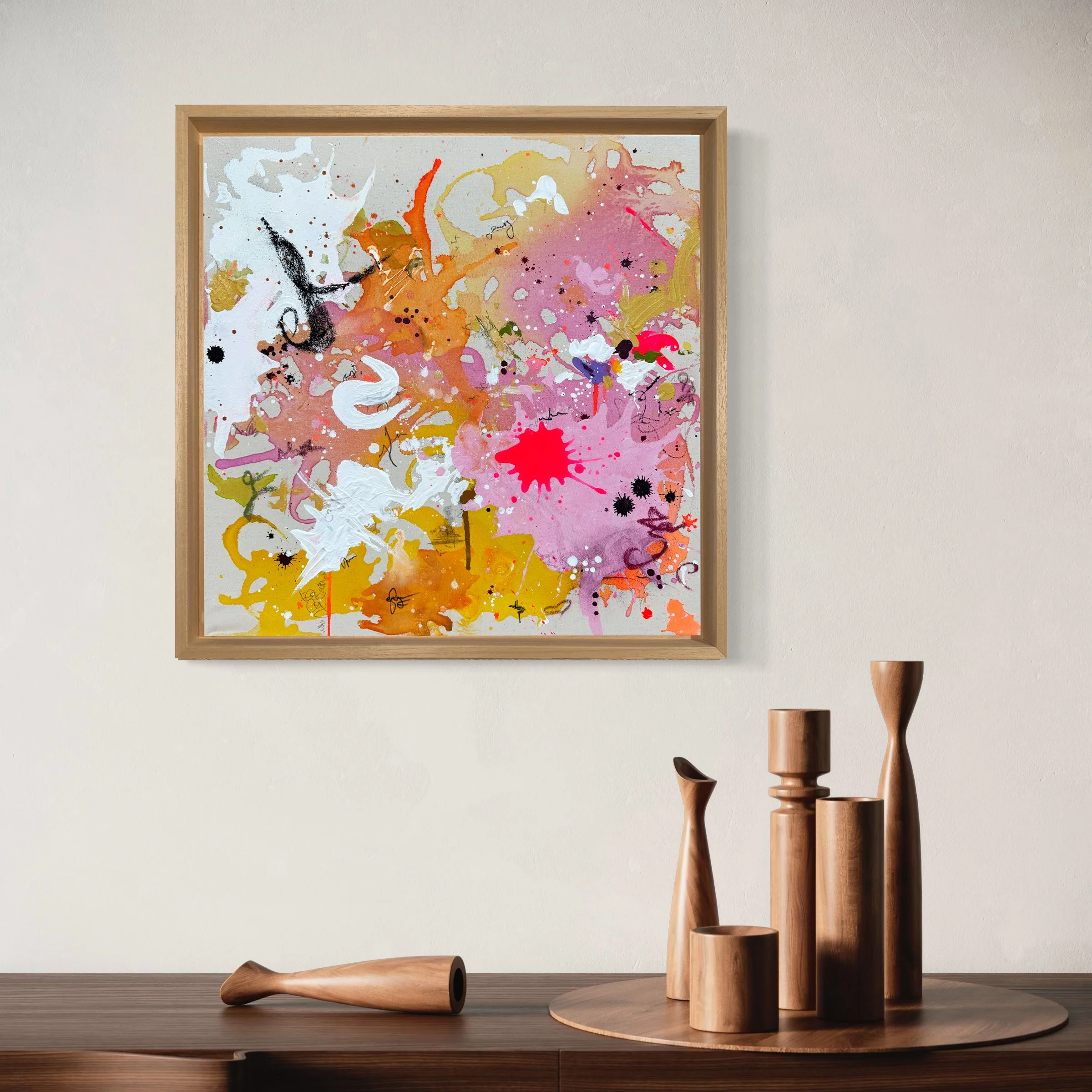Abstraktes Gemälde mit bunten Farbklecksen und Spritzern in einem Holzrahmen, an einer weißen Wand, mit Holzskulpturen auf einem Tisch davor