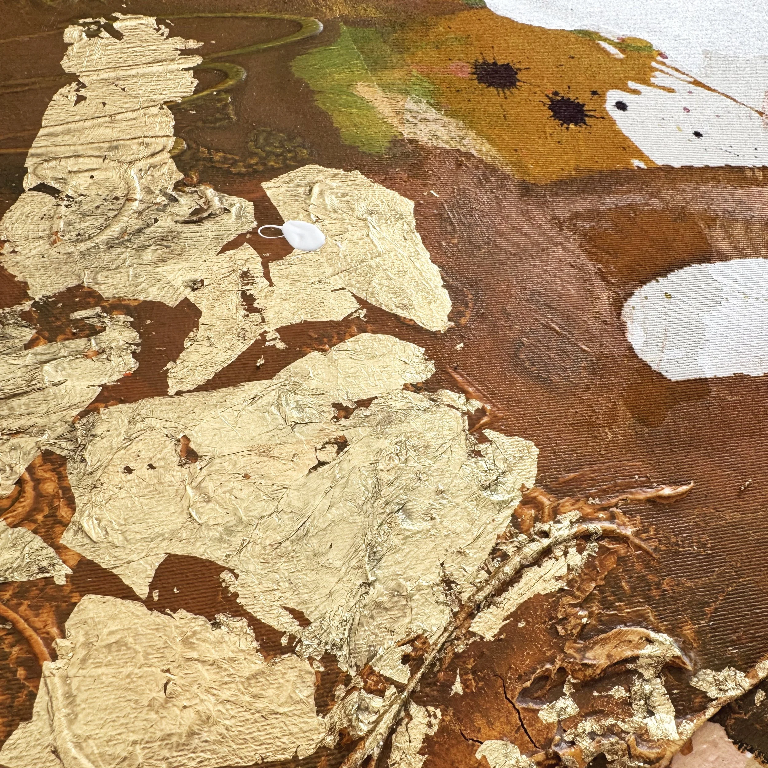 Tiefstehendes Bild eines Künstlers zeigt Blattgold im Kontrast zu einer bunten Leinwand mit Farbklecksen, die eine kreative Mal-Szene darstellen.