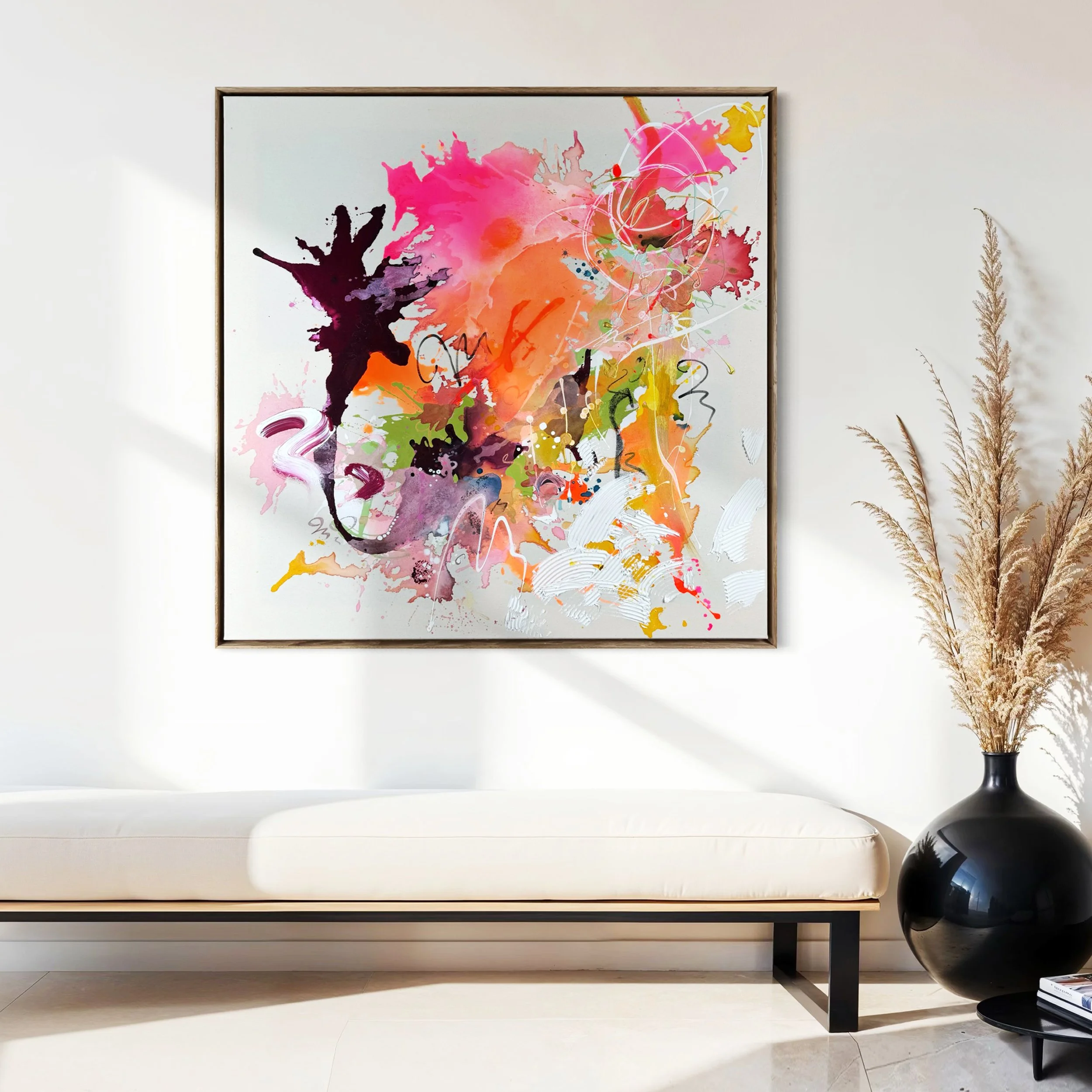 Ein modernes abstraktes Gemälde mit bunten Farbklecksen an einer weißen Wand über einem weißen Sofa, mit einer schwarzen Vase voller getrockneter Gräser daneben.