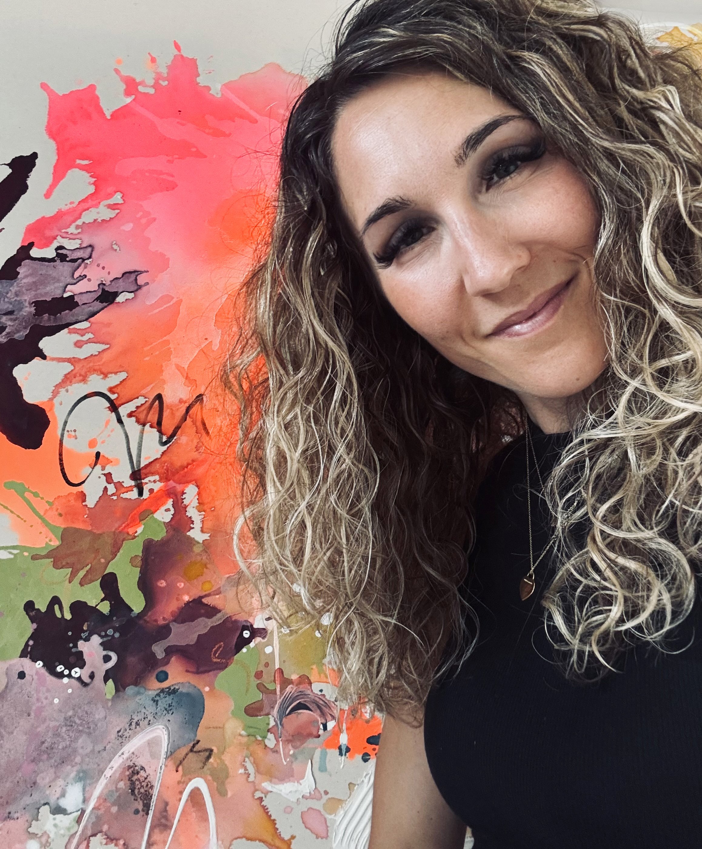 Frau mit lockigem Haar, lächelnd, neben abstrakter, bunter Wandmalerei.