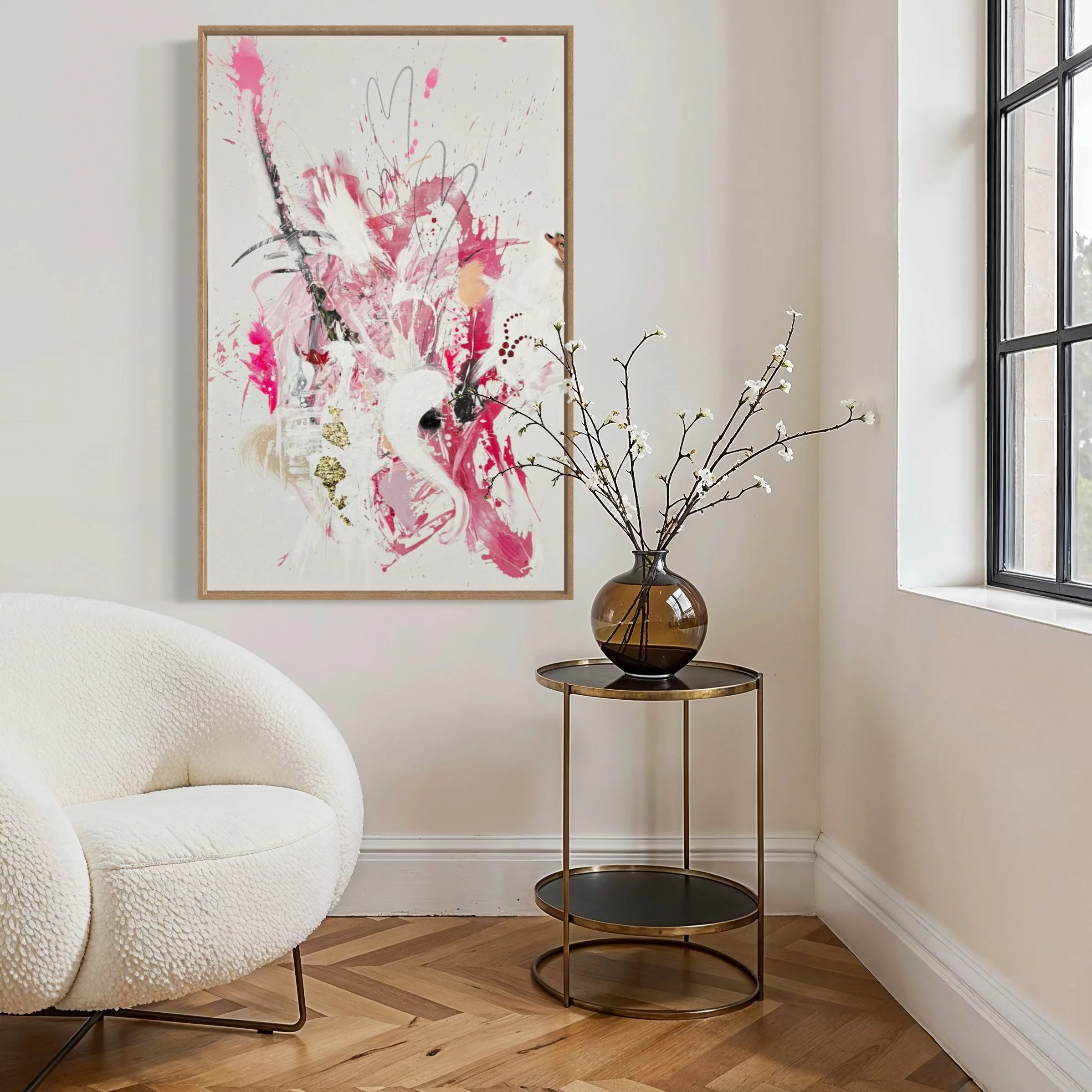 Ein helles, modernes Wohnzimmer mit einer weißen, wolligen Couch, einem runden Beistelltisch mit einer braunen Vase und weißen Zweigen, einer großen abstrakten Farbgebung an der Wand, und einem Fenster auf der rechten Seite.