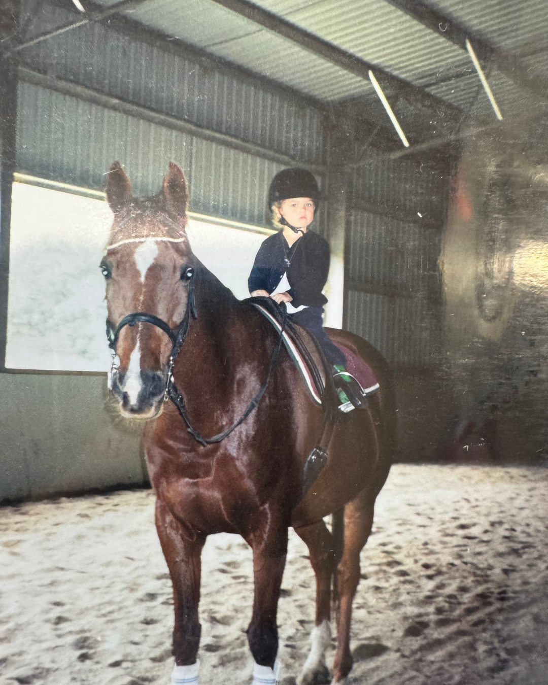 Young child in equestrian helmet riding a brown horse inside a riding arena.