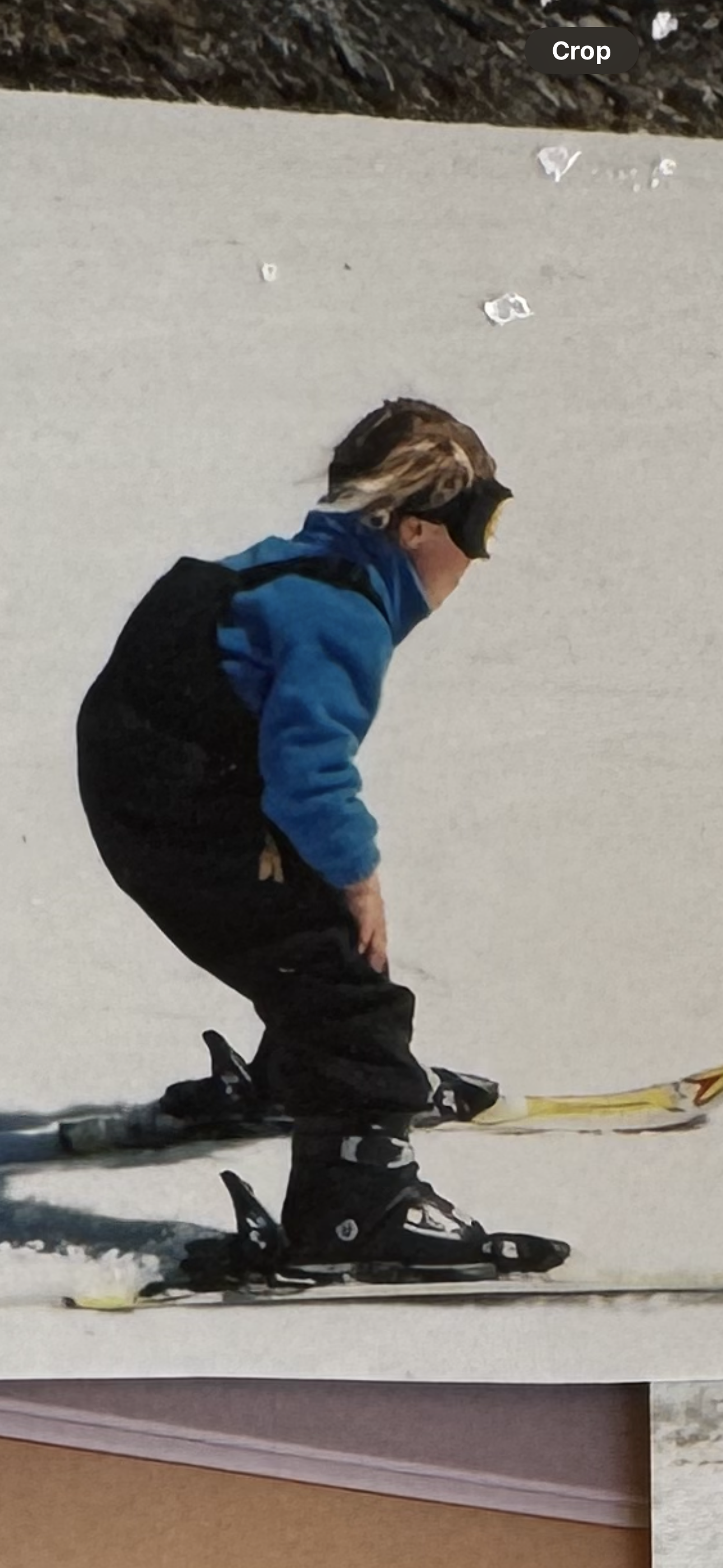 Child in blue jacket and black ski pants skiing on snow, wearing a helmet and goggles.