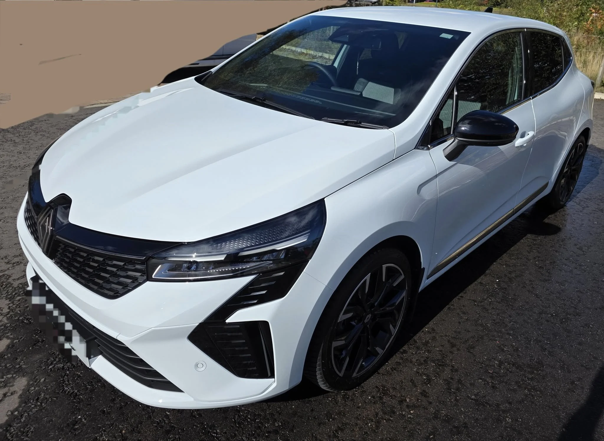 White hatchback car parked on a gravel surface, with black rims and tinted windows.