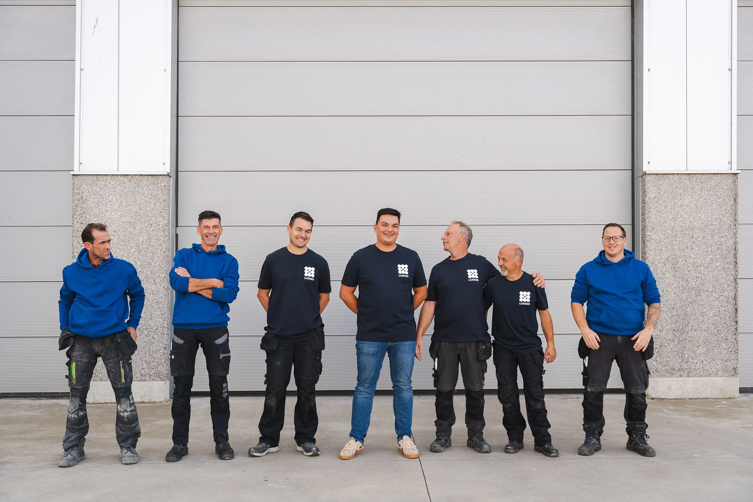 Medewerkers van Ludiso in Bilzen-Hoeselt lachen samen tijdens een informele teamfoto voor de productiehal