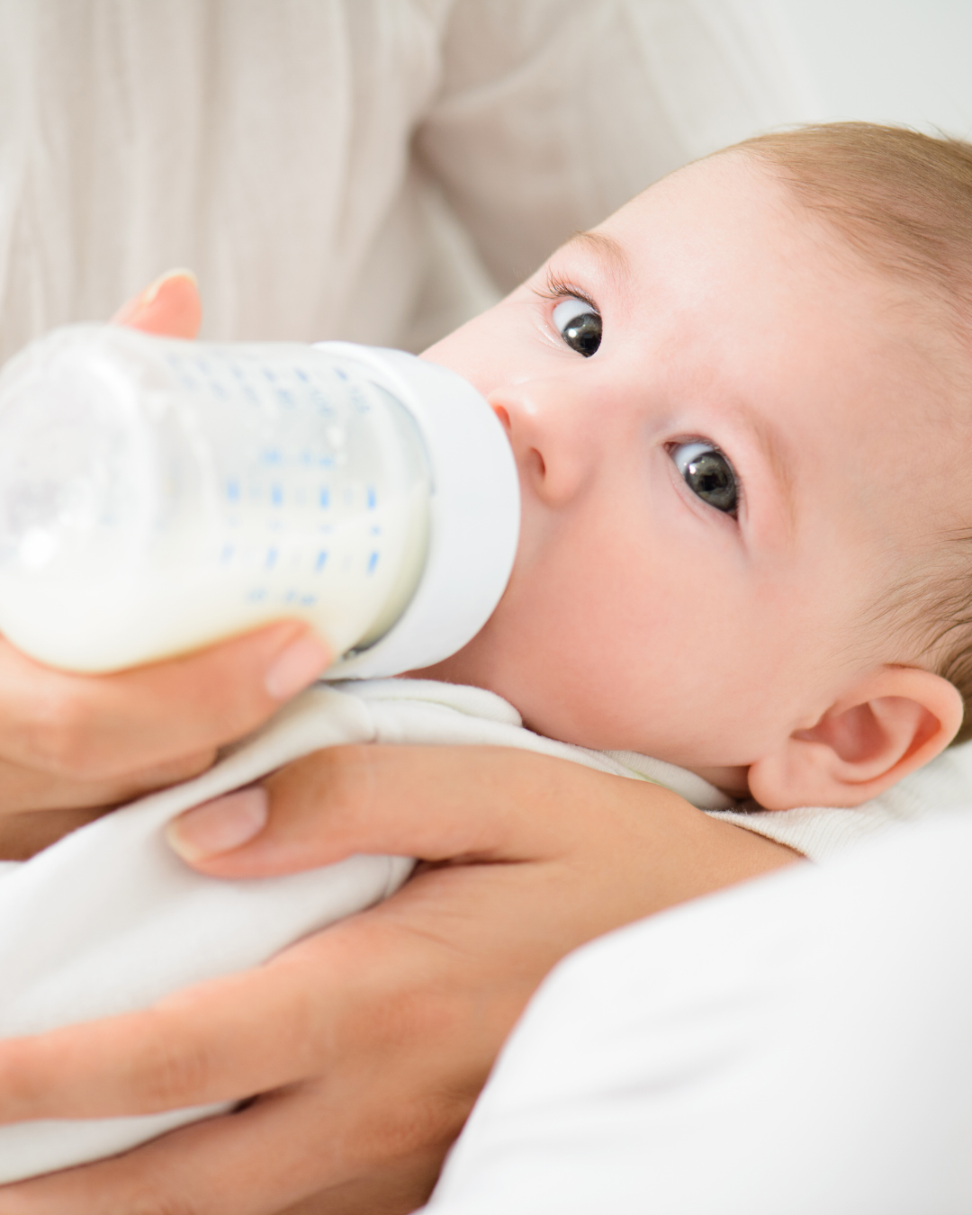 Close-up of a baby lying on an adult's arms, drinking milk from a bottle.