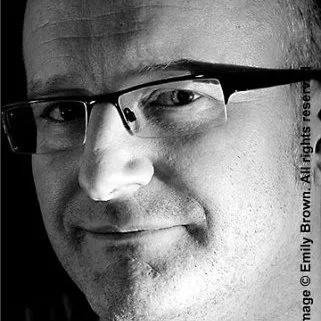 Close-up of a man wearing glasses, smiling slightly.