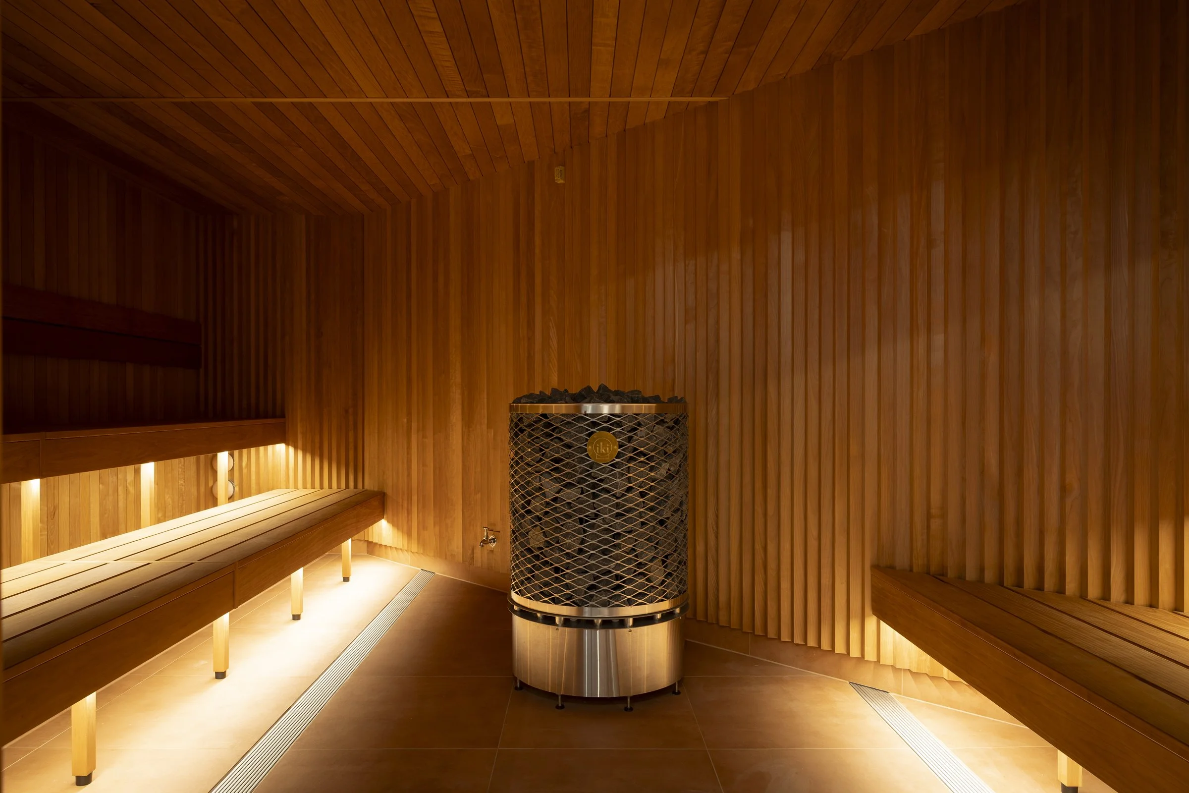 A secluded glass-front infrared sauna room with wooden interior walls, benches, and a heater filled with stones.