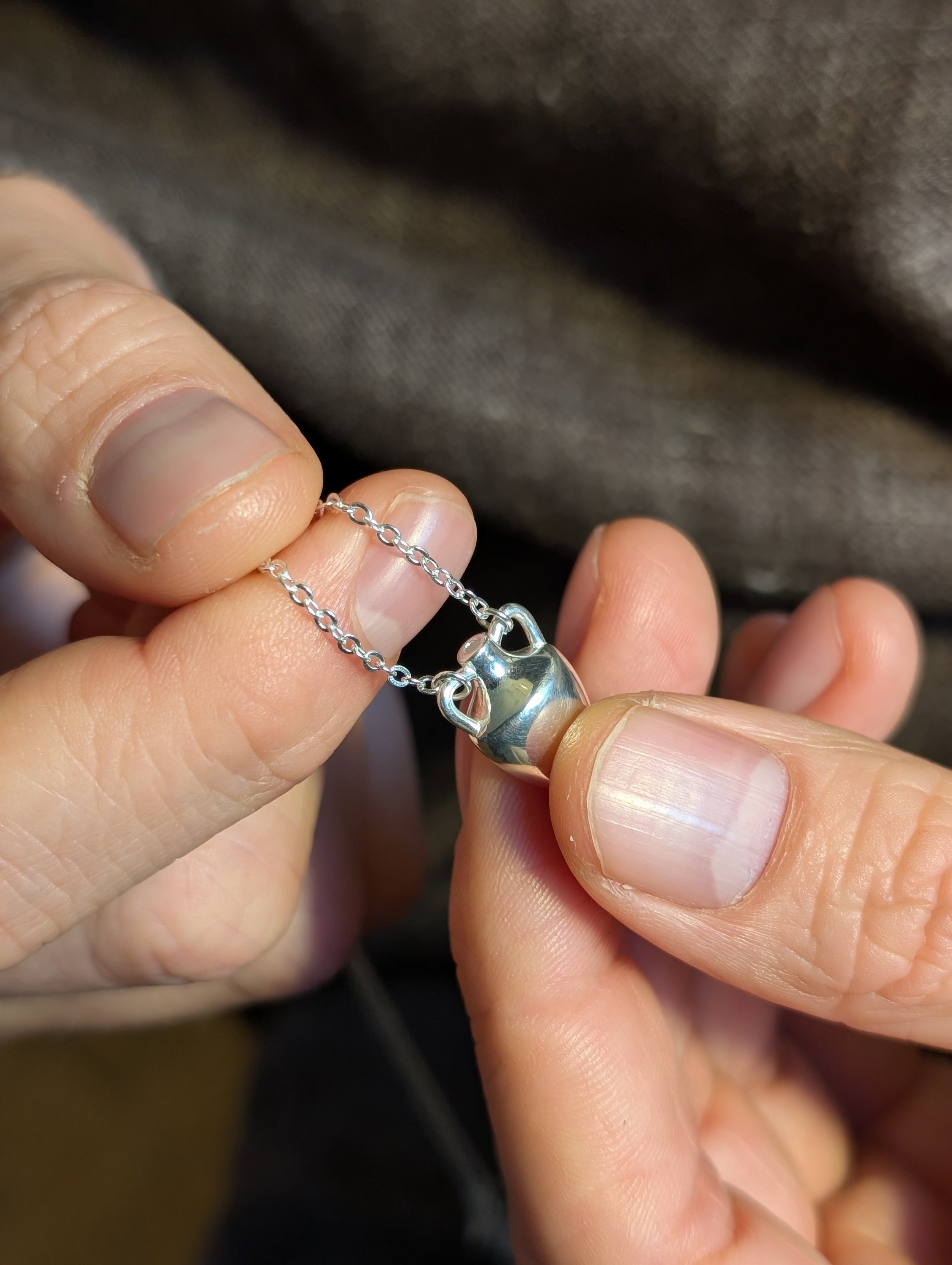 Close-up of a person holding a silver necklace with an amphora shaped pendant.