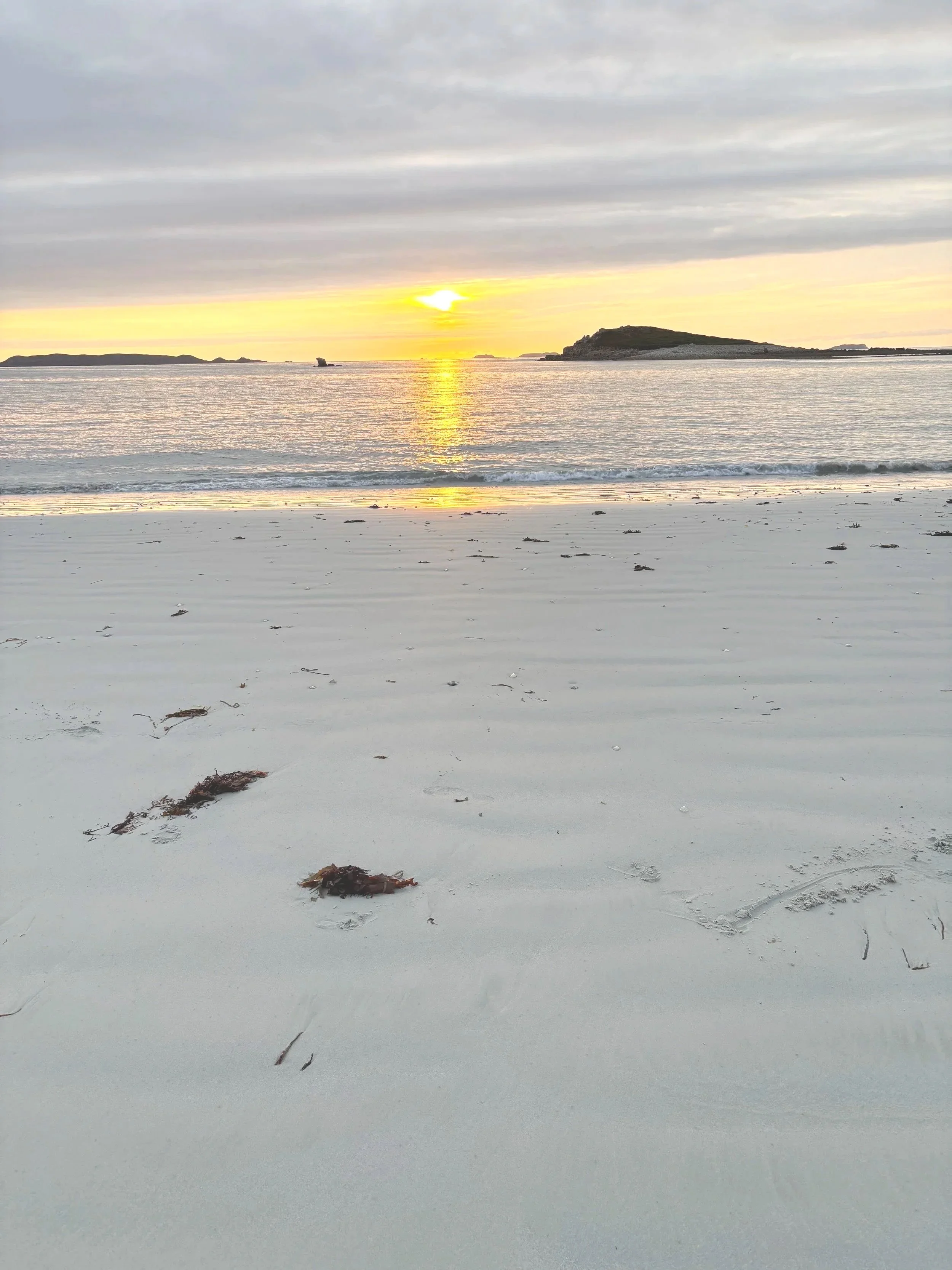Coucher de soleil sur une plage de sable blanc avec des îles au loin, dans le ciel nuageux.