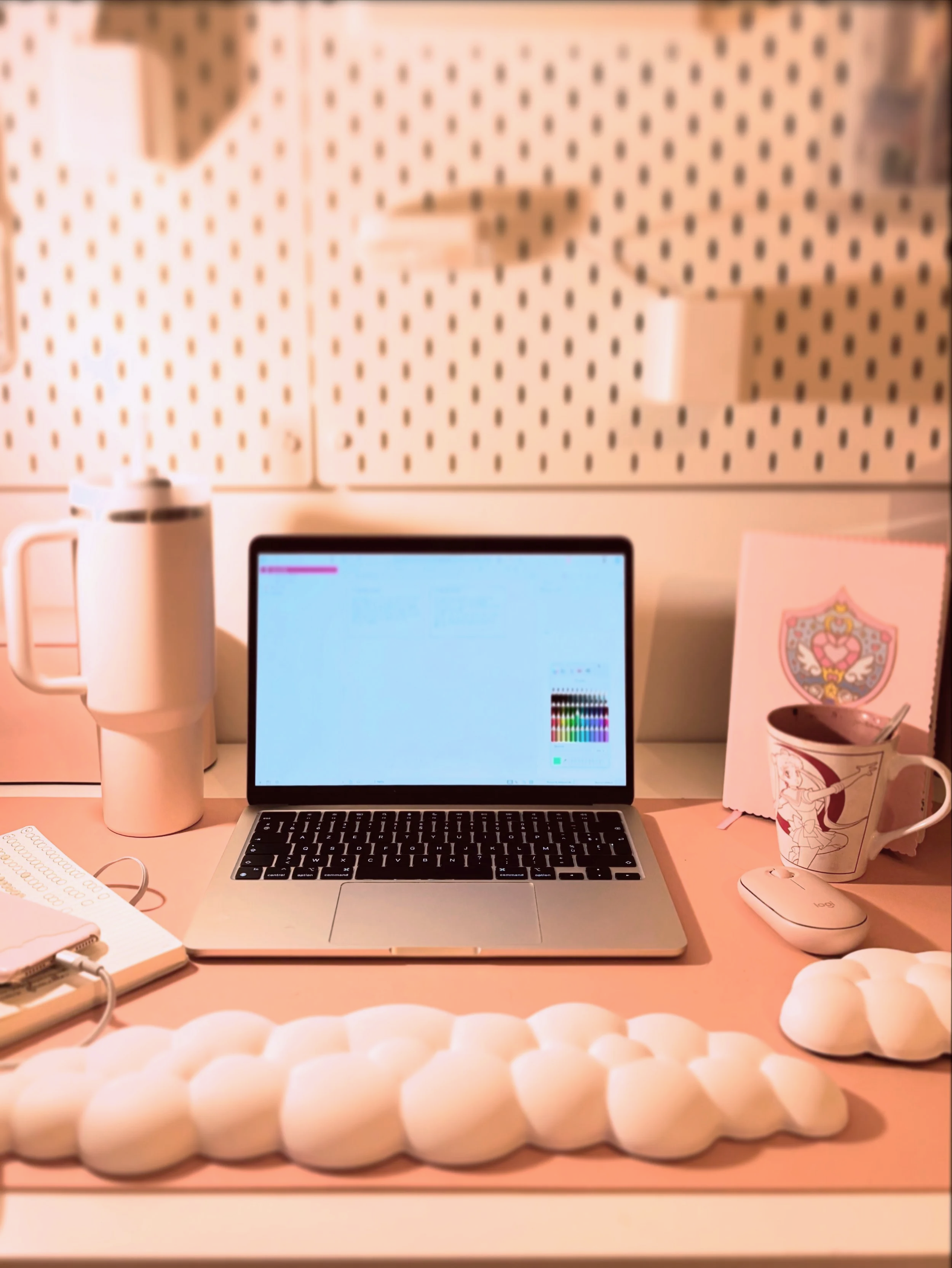 Bureau avec un ordinateur portable, une tasse à café avec une cuillère, une liseuse, une souris, un carnet, un porte-stylo, et une pelote de laine blanche, dans un espace de travail ou bureau.