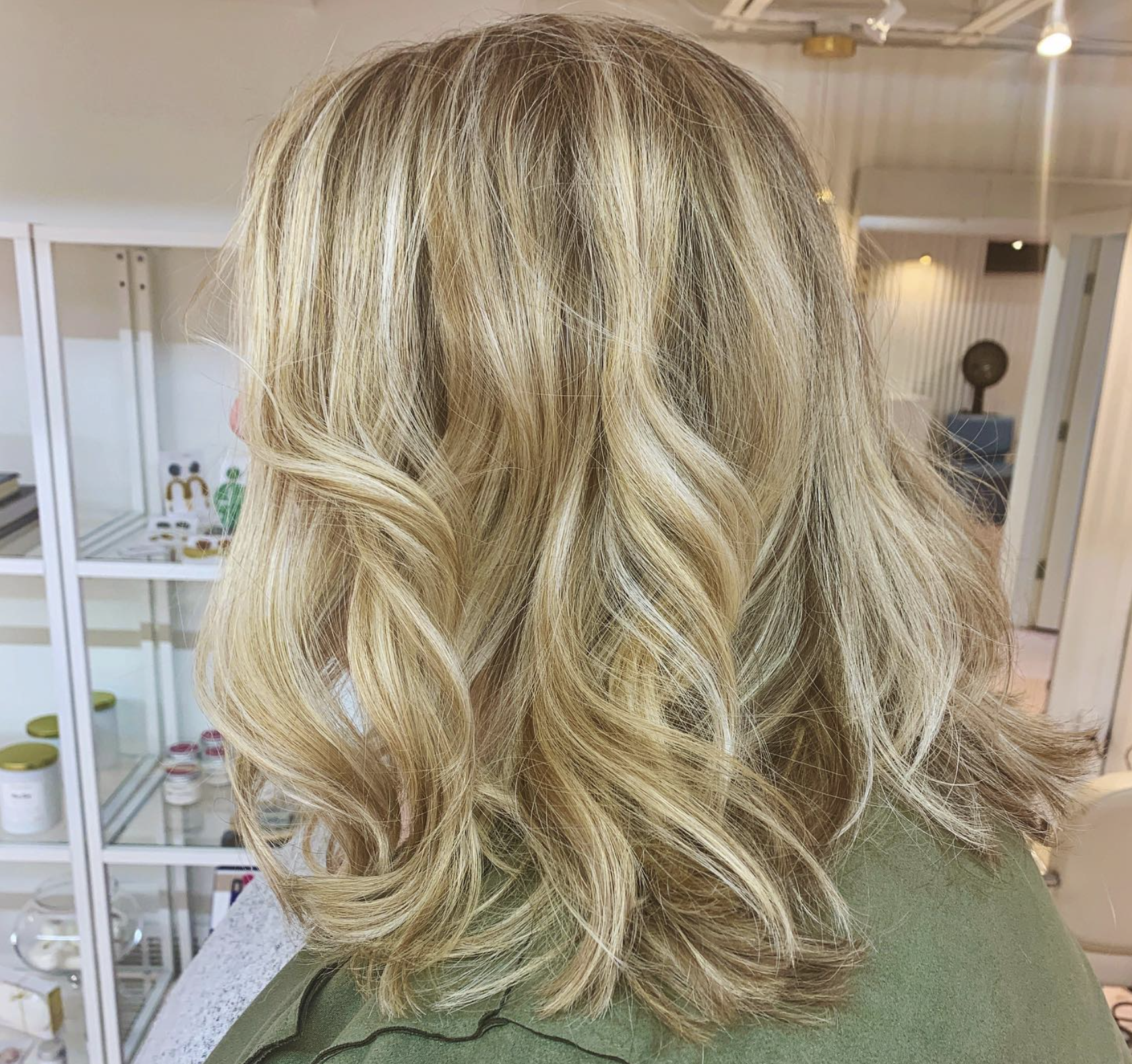Woman with shoulder-length blonde wavy hair in a salon setting.