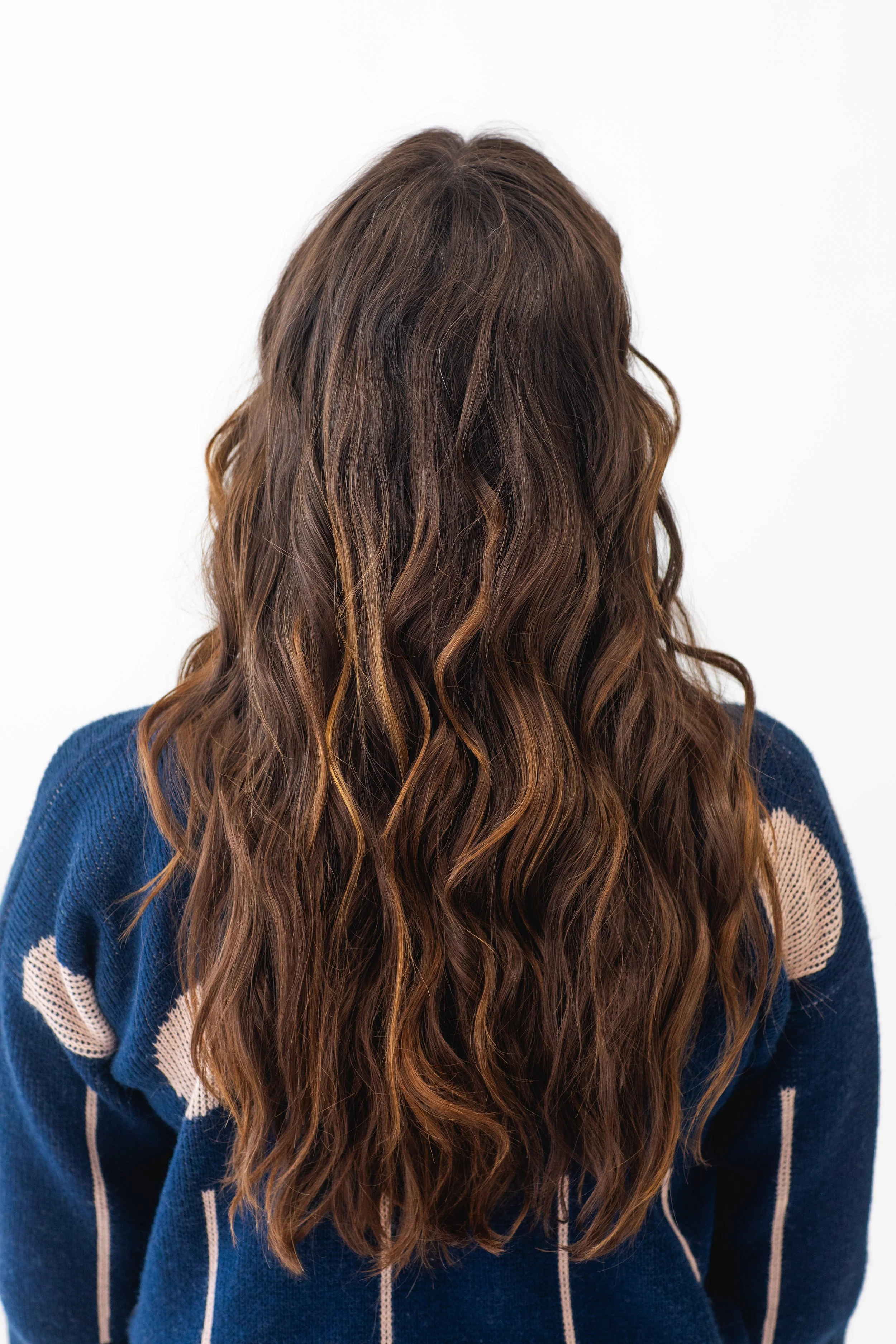 A back view of soft, flowing brunette waves with subtle golden ribbons of color. This style shows the depth and dimension created through hand-painted highlights, ideal for clients wanting a natural, beachy finish. brunette balayage, dimensional brun