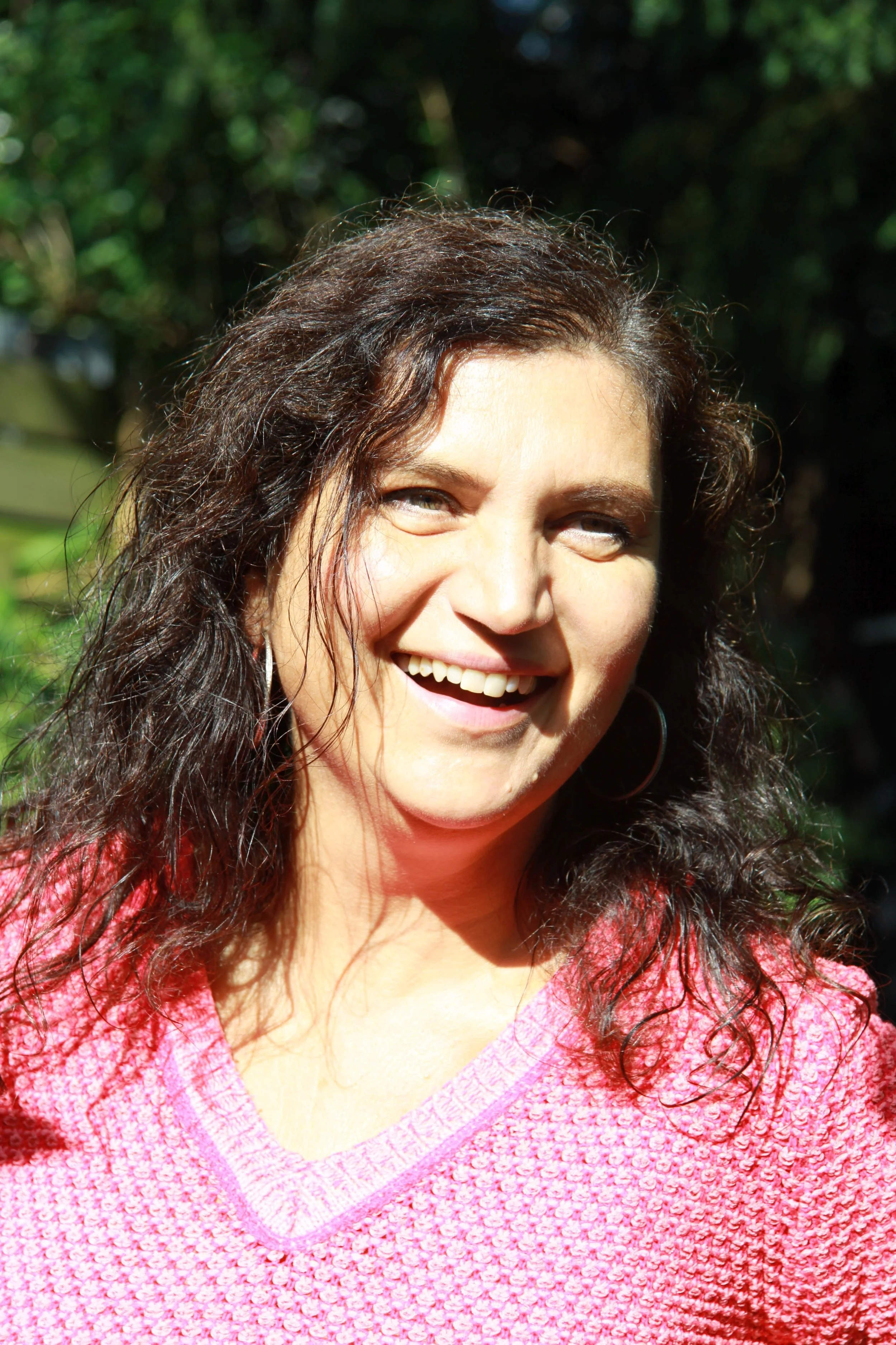 Bianca Alexandra Kampa mit braunen, lockigen Haaren in einem pinken Pullover im Freien bei Sonnenschein.