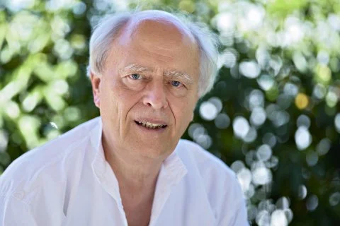 Ingo Jahrsetz. Ein älterer Mann mit weißen Haaren und blauer Augen, trägt ein weißes Hemd, steht vor einem grünen, blühenden Hintergrund.