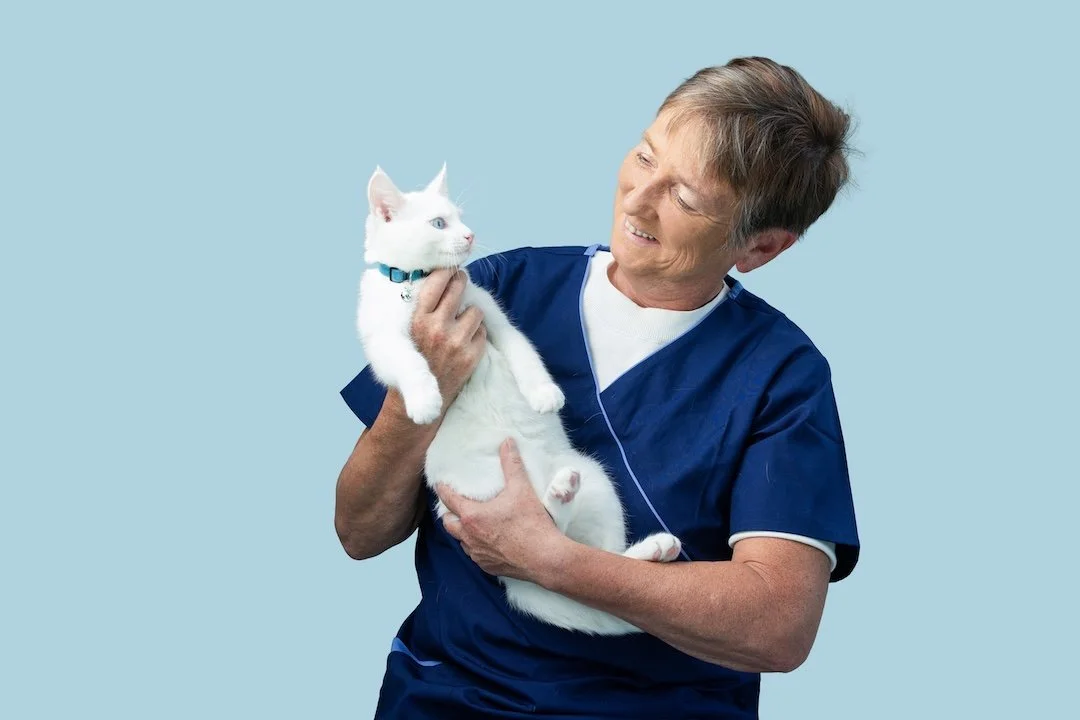 Older man smiling and holding a Siamese cat outdoors in a garden.