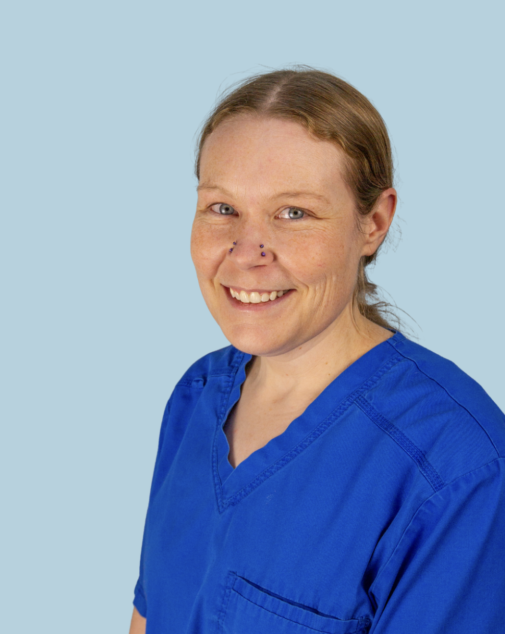 A vet wearing blue medical scrubs, smiling, against a light blue background.